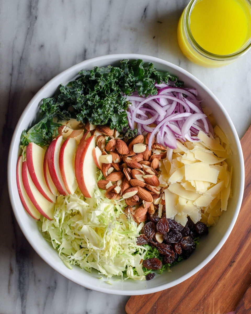 A white bowl filled with six separate layers of salad ingredients is shown from above on a white marbled surface. Starting from the top and moving clockwise, there is a layer of dark green curly kale, thin slices of red apple with white flesh and red edges, thinly sliced purple onions, a pile of roasted almonds with a rough texture, shredded light green cabbage, and a small group of dark brown raisins next to shaved pale yellow cheese pieces. To the upper right of the bowl, a small glass jar contains bright yellow dressing. Photo taken with an iphone --ar 4:5 --v 7