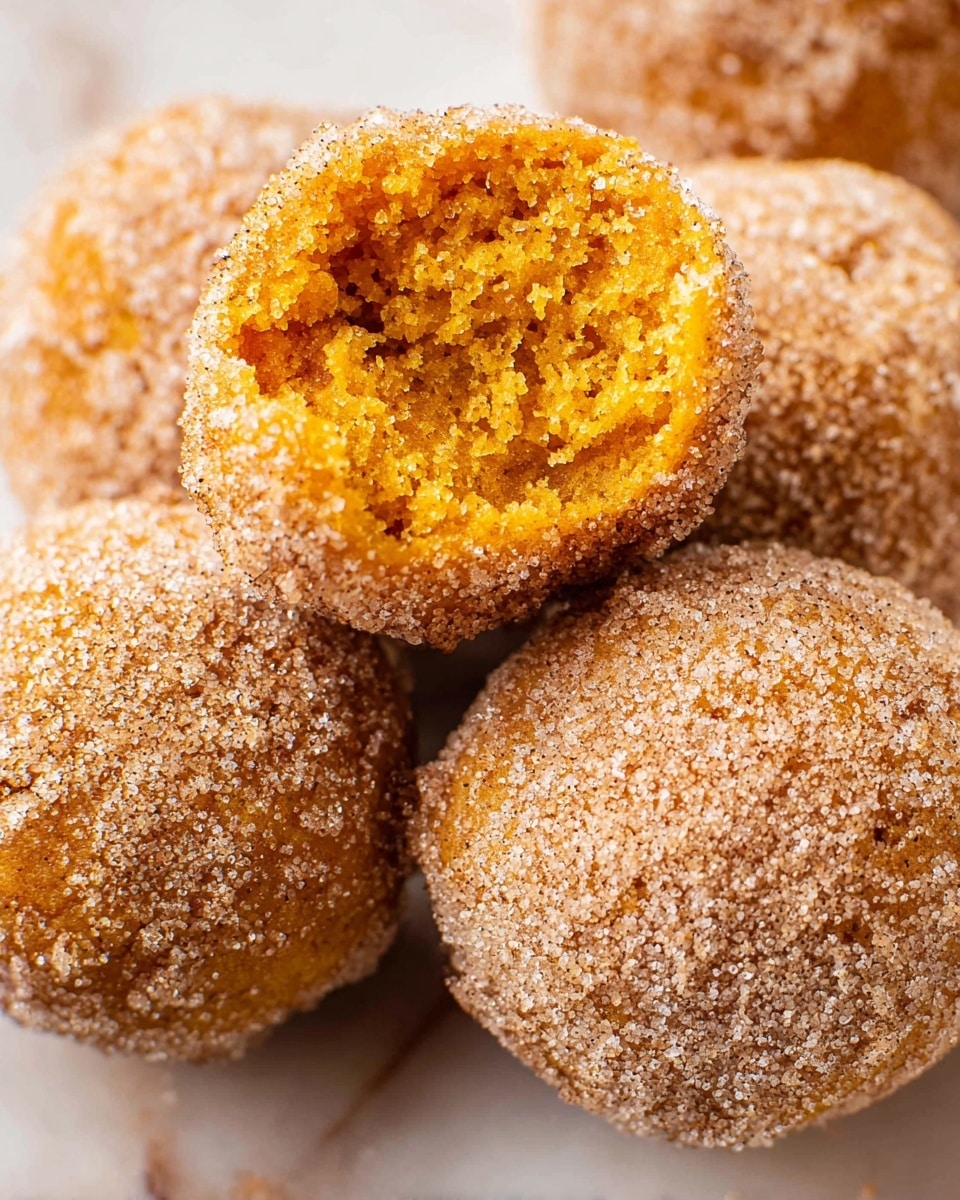 A close-up view of four round doughnut holes on a white marbled surface. Three doughnut holes are whole, coated in a grainy layer of cinnamon sugar that sparkles with a light tan and white mix. The fourth doughnut hole is broken open and placed on top, showing a soft, crumbly texture inside with a bright orange-yellow color. The rough sugar coating contrasts with the moist, porous inside. The overall look is warm and inviting, with a focus on texture and color contrast. Photo taken with an iphone --ar 4:5 --v 7