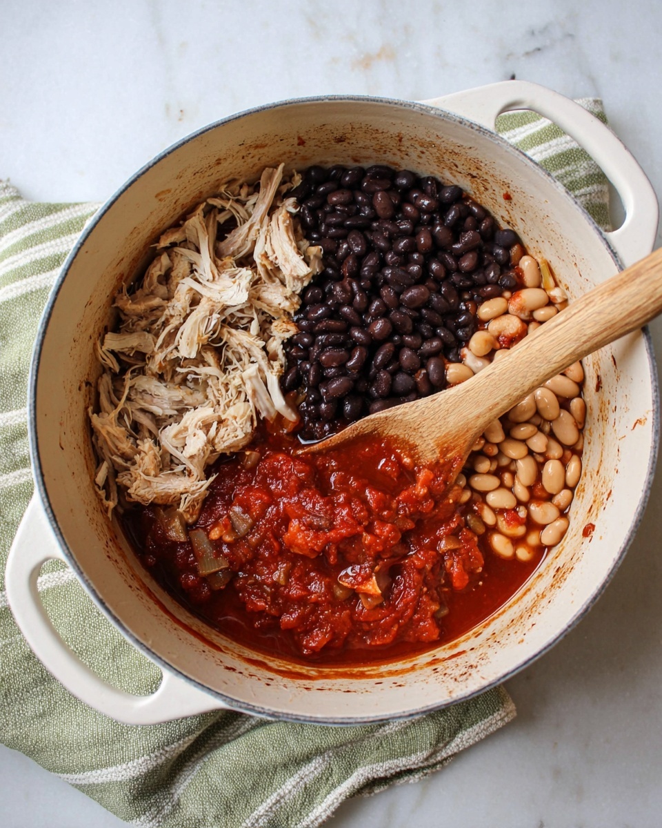 A white oval pot sits on a white marbled surface with a striped green and white cloth under the right side. Inside the pot, the food is divided into four distinct sections: the top left section has shredded pale beige meat, the top middle is filled with shiny black beans, the top right holds light brown beans, and the bottom section has a thick, chunky deep red sauce with visible small pieces. A light wooden spoon rests inside on the left side, partially submerged in the sauce. The pot's edges show slight browning marks from cooking. Photo taken with an iphone --ar 4:5 --v 7