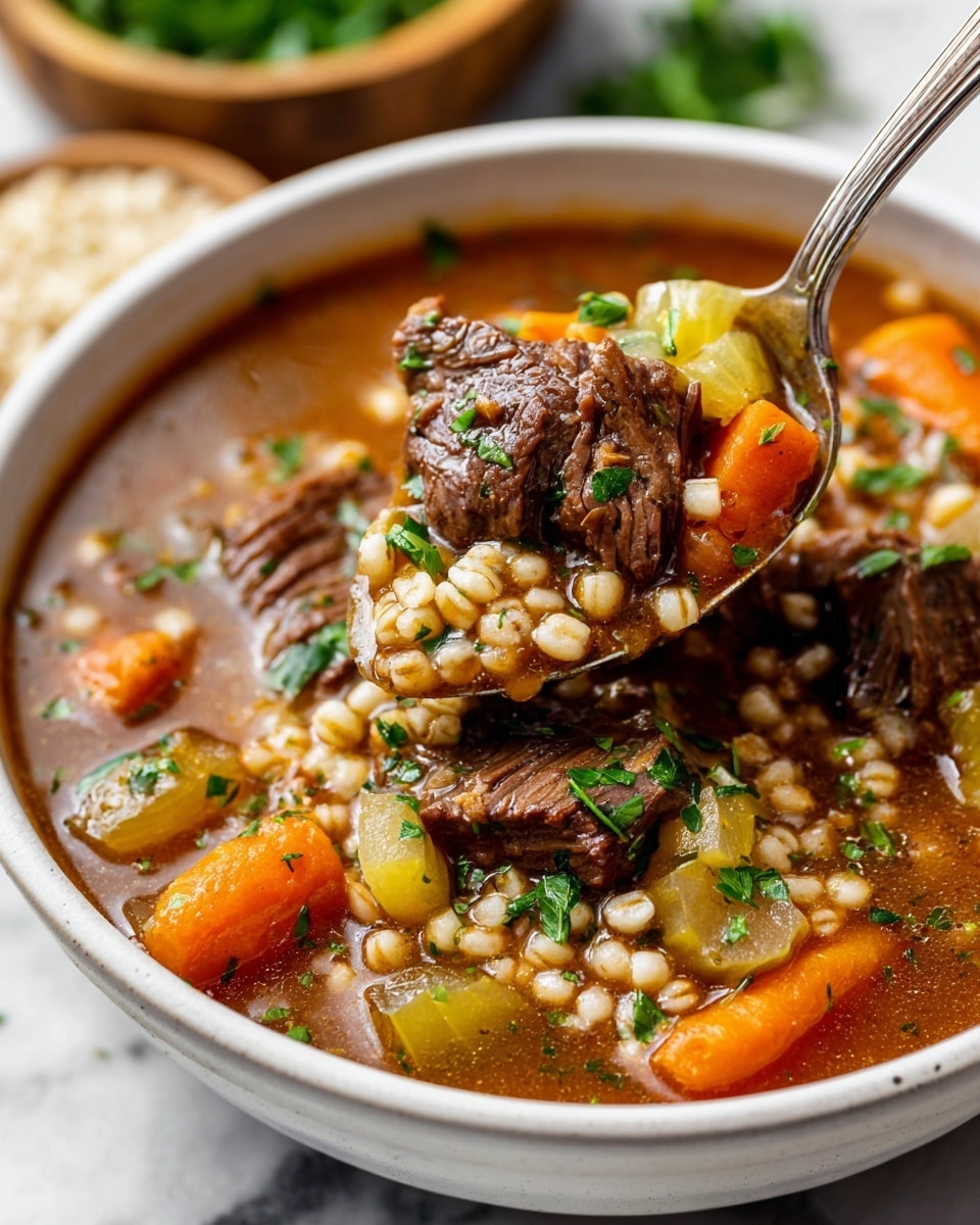 A close-up of a white bowl filled with a hearty soup made of dark brown beef chunks, orange carrot slices, light green celery pieces, and pale pearl barley grains in a rich brown broth. Bright green parsley is sprinkled on top, adding fresh color. A metal spoon in the bowl lifts a piece of beef and some vegetables above the soup, showing the texture and colors clearly. The bowl sits on a white marbled surface, with blurred fresh parsley and grains in a wooden bowl in the background. Photo taken with an iphone --ar 4:5 --v 7
