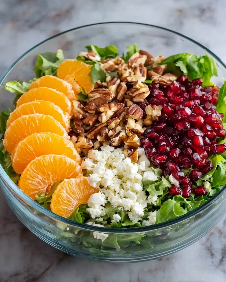 A clear glass bowl filled with a colorful salad is shown. The bottom layer consists of fresh green mixed leafy vegetables. On top of the greens, there are four distinct sections: bright orange mandarin slices on the left, white crumbled cheese next to the mandarins, chopped brown nuts beside the cheese, and shiny red pomegranate seeds on the far right. The clear glass bowl sits on a white marbled surface photo taken with an iphone --ar 4:5 --v 7