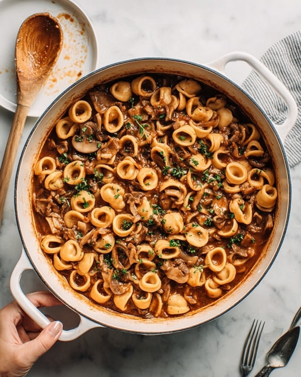 A white pot filled with several layers of small round pasta rings mixed with a chunky brown sauce, small pieces of mushrooms, and bits of green herbs scattered on top. The pot is placed on a white marbled surface, with a woman's hand holding the pot handle. Nearby, there is a wooden spoon with sauce stains and a small white plate with a silver fork resting on it. photo taken with an iphone --ar 4:5 --v 7