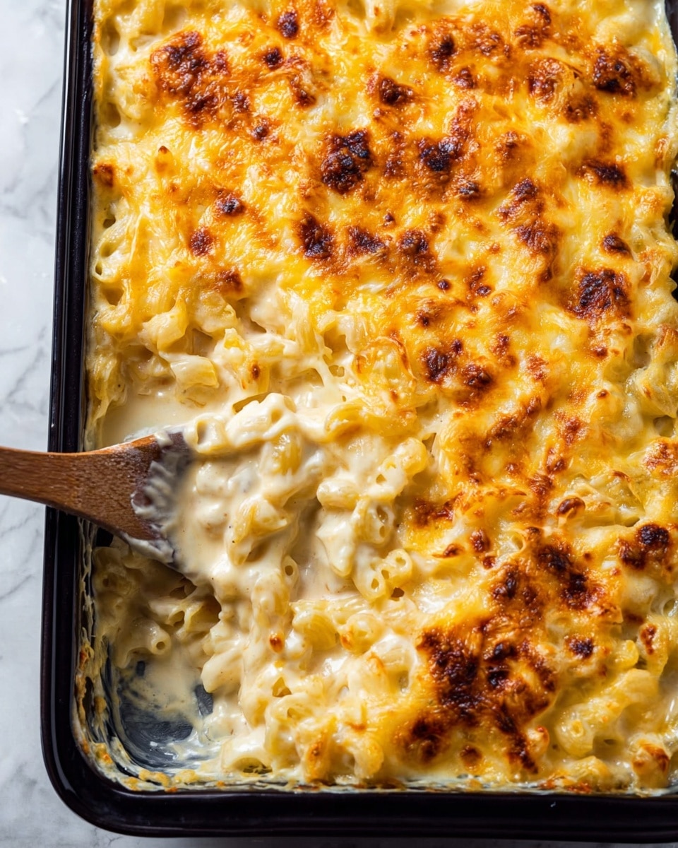 A rectangular black baking dish filled with creamy macaroni and cheese, showing one main layer of elbow pasta coated in smooth, pale yellow cheese sauce. The top layer is golden yellow melted cheese with a slightly browned, bubbly texture scattered unevenly across the surface. In one corner, a wooden spoon is scooping out a portion, lifting the creamy pasta mix from below the crispy cheese crust. The baking dish is set on a white marbled surface. Photo taken with an iphone --ar 4:5 --v 7