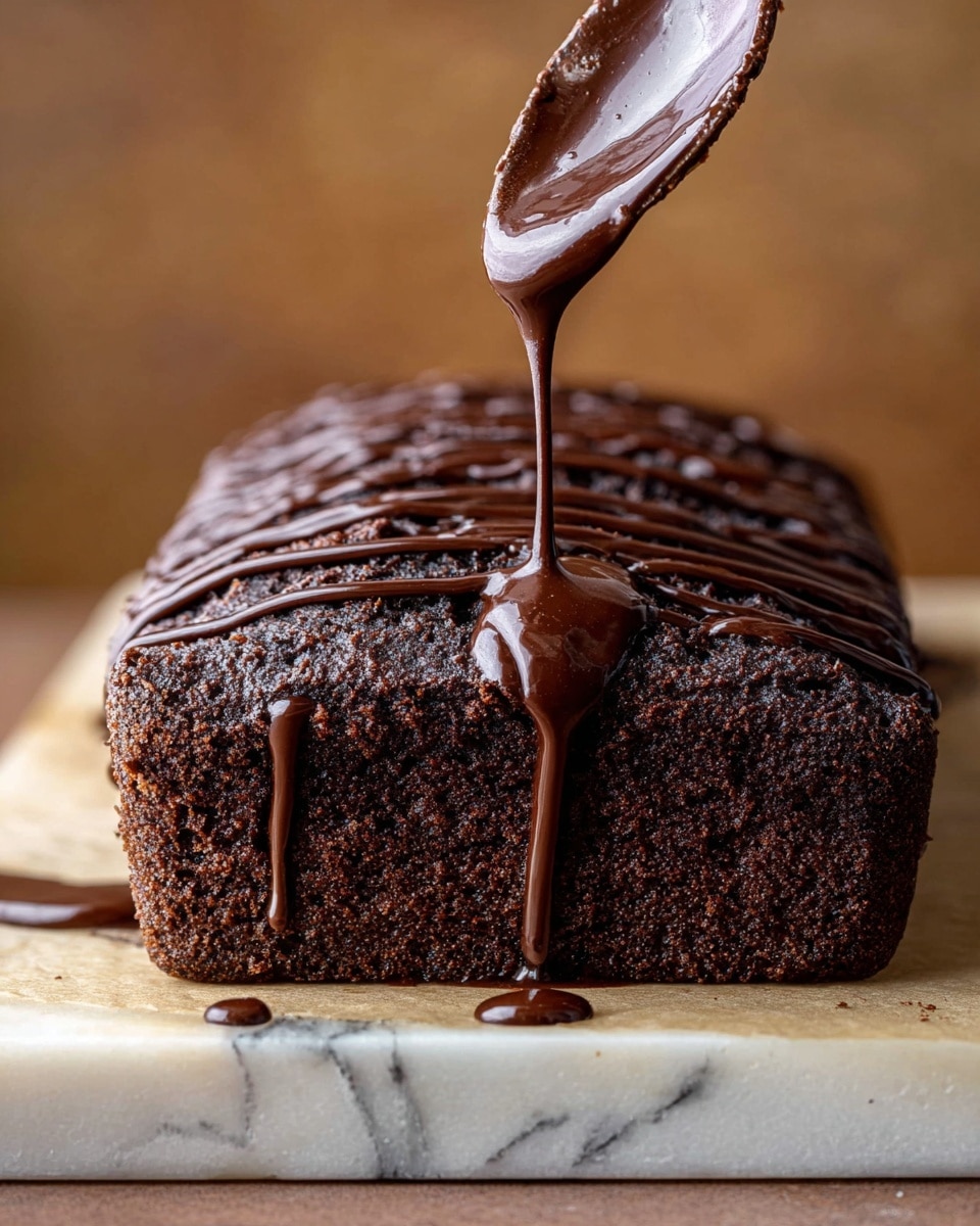A dark brown chocolate cake loaf with a rough, crumbly texture sits on a flat surface with a white marbled texture. Thick, glossy chocolate sauce is being poured from a spoon onto the top right side of the loaf, forming thick shiny drips that run down the front and side surfaces. There are already several straight lines of the same chocolate sauce drizzled on the top left side of the cake, contrasting with the matte cake texture. Some drops of chocolate sauce have fallen on the surface near the cake. The background is softly blurred in warm tones. Photo taken with an iphone --ar 4:5 --v 7