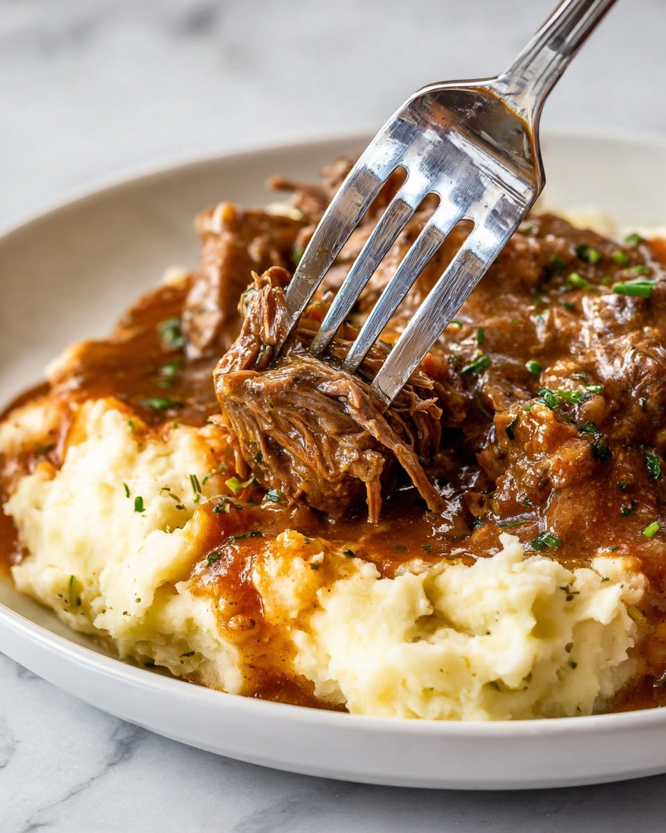 The image shows a close-up of a white plate with two main layers: the bottom layer is soft, creamy mashed potatoes with a light texture and pale yellow color. On top, there is a rich layer of brown stew with tender pieces of meat covered in a thick sauce, speckled with small green herb bits. A shiny fork is pressing into a piece of the meat, lifting it slightly above the mashed potatoes. The plate sits on a white marbled surface, and the colors focus mainly on brown and light cream with hints of green from the herbs. photo taken with an iphone --ar 4:5 --v 7