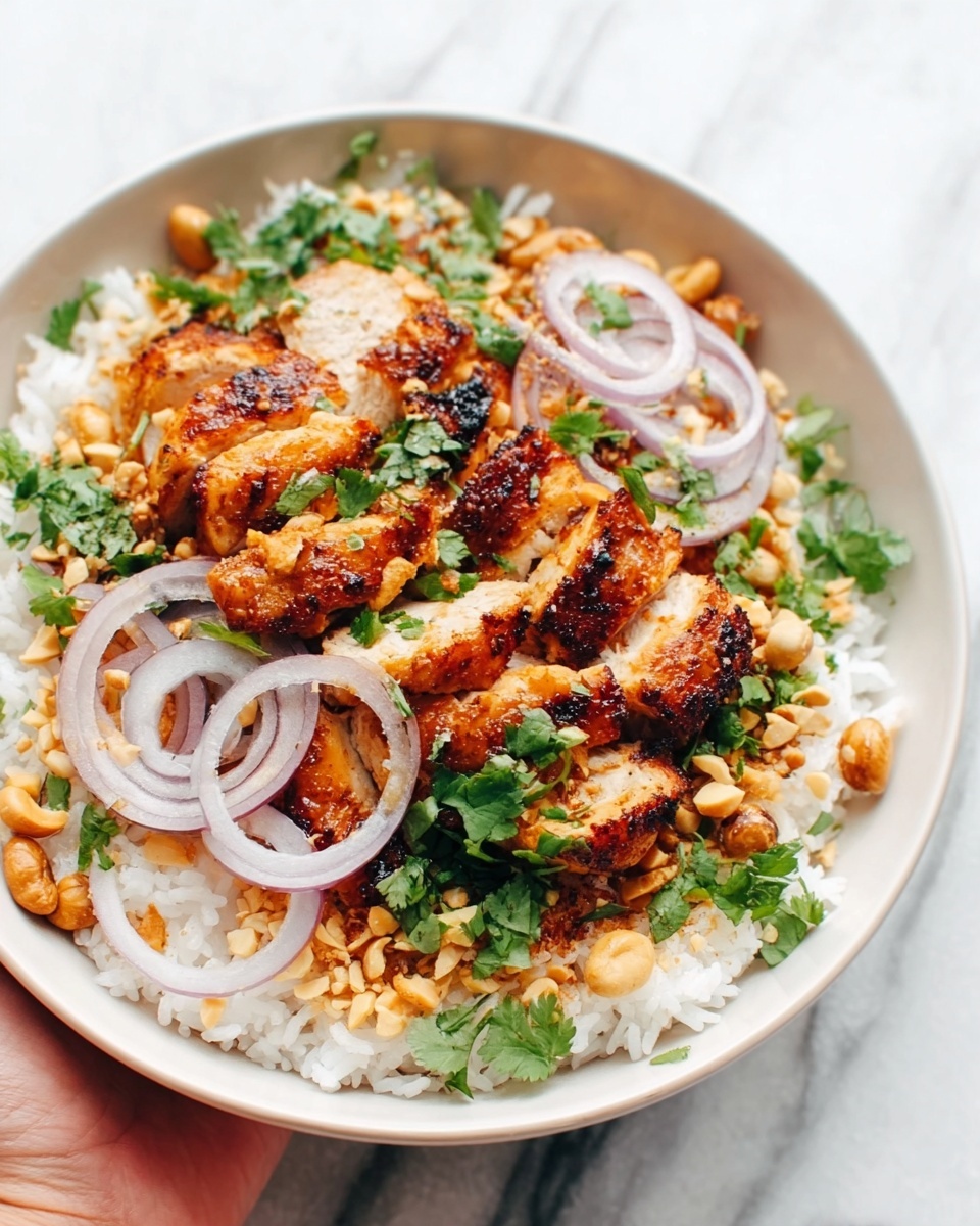 The image shows a white bowl filled with layers of food on a white marbled surface. At the bottom, there is a base of fluffy white rice. On top of the rice, there are pieces of golden brown grilled chicken arranged in the center. Around the chicken, slices of light purple onion rings and chopped green herbs add color. The dish is sprinkled with crushed peanuts and small green chopped herbs all over. A woman's hand with light skin is holding the bowl from the side. The colors are warm and fresh with textures from smooth rice, soft onions, and crunchy peanuts. The photo is clear and bright, showing the details nicely. photo taken with an iphone --ar 4:5 --v 7