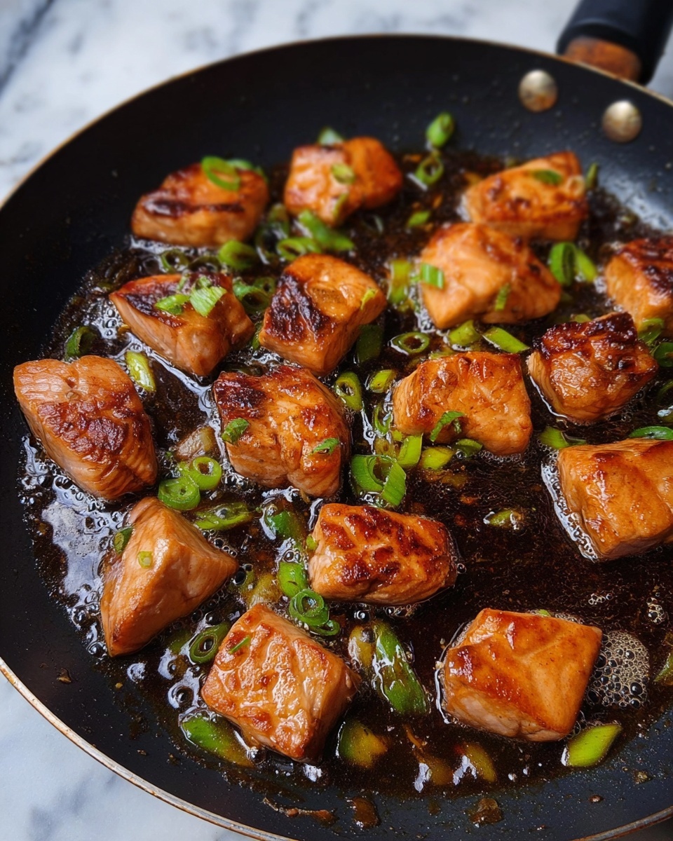 The image shows a black frying pan filled with about sixteen small, browned salmon pieces cooking in a glossy, dark sauce with green onion slices scattered around. The salmon pieces are golden-brown on the outside with a slightly seared texture and are unevenly placed across the pan. Some sauce bubbles gently around the pieces, adding shine and moisture. The background features a white marbled texture, and the overall lighting highlights the rich colors and textures of the salmon and sauce. photo taken with an iphone --ar 4:5 --v 7