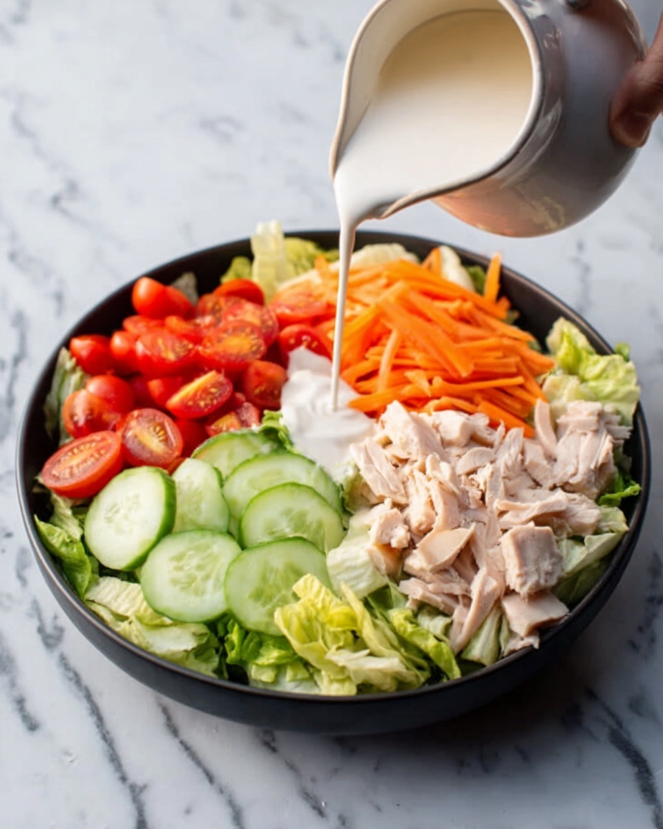 A black bowl on a white marbled surface holds a colorful layered salad. At the bottom left, there is a bed of light green lettuce. On top of this, sliced cucumbers form the bottom middle layer with a smooth green surface. To the upper left, there are bright red cherry tomato halves arranged in a small group. On the right side, pieces of light pink cooked chicken are layered near the center. Above the chicken, there are thin, orange carrot strips. A white creamy sauce is being poured over the chicken from the top right, creating a contrast against the other colors. A woman's hand is holding a white pitcher from which the sauce flows. Photo taken with an iphone --ar 4:5 --v 7