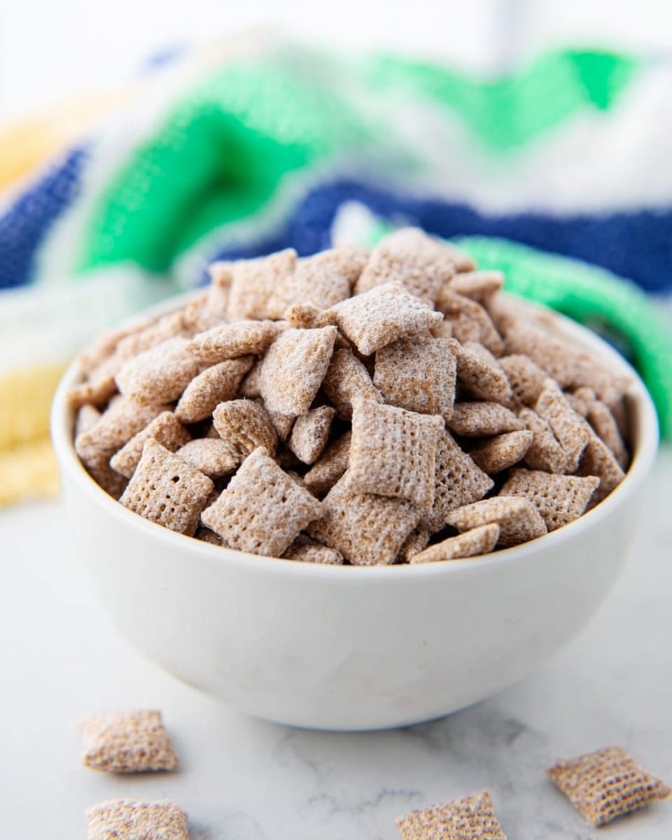 A white bowl filled with many small square cereal pieces that are light brown and covered in a powdery coating. The cereal pieces are stacked tightly above the bowl's rim, showing their soft texture and tiny holes on some pieces. The bowl sits on a white marbled surface with a blurred cloth in blue, green, white, and yellow stripes placed next to it. Photo taken with an iphone --ar 4:5 --v 7