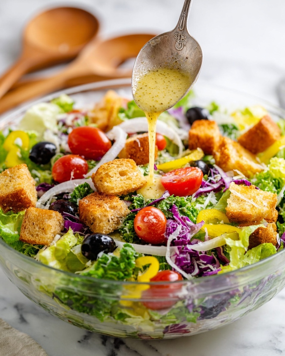 The image shows a fresh salad in a clear glass bowl on a white marbled surface. The salad has several layers starting with bright green leafy lettuce mixed with shredded purple cabbage and thin slices of white onion. On top, there are halved red cherry tomatoes, black olives, and yellow pepper rings scattered evenly. Golden-brown crunchy croutons are placed on the surface, adding texture. A creamy light yellow dressing is being poured from a silver spoon onto the salad, visible in mid-air as it drips down slowly. In the background, two wooden salad serving spoons rest against the bowl. Photo taken with an iphone --ar 4:5 --v 7