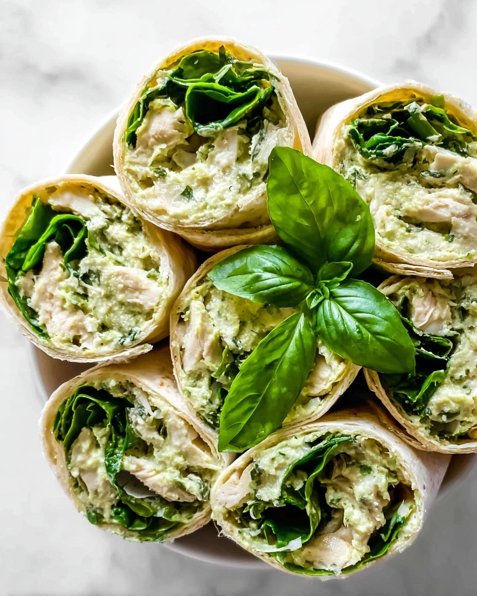 The image shows a close-up of several wrap pieces arranged in a circle on a white bowl, placed on a white marbled surface. Each wrap has a soft, light beige tortilla outer layer, filled inside with a creamy, pale green mixture that looks smooth with small chunks, layered with bright fresh green spinach leaves and small pieces of white chicken. Bright green basil leaves are placed in the center for decoration. The textures of the creamy filling contrast with the fresh crispness of the spinach leaves. photo taken with an iphone --ar 4:5 --v 7