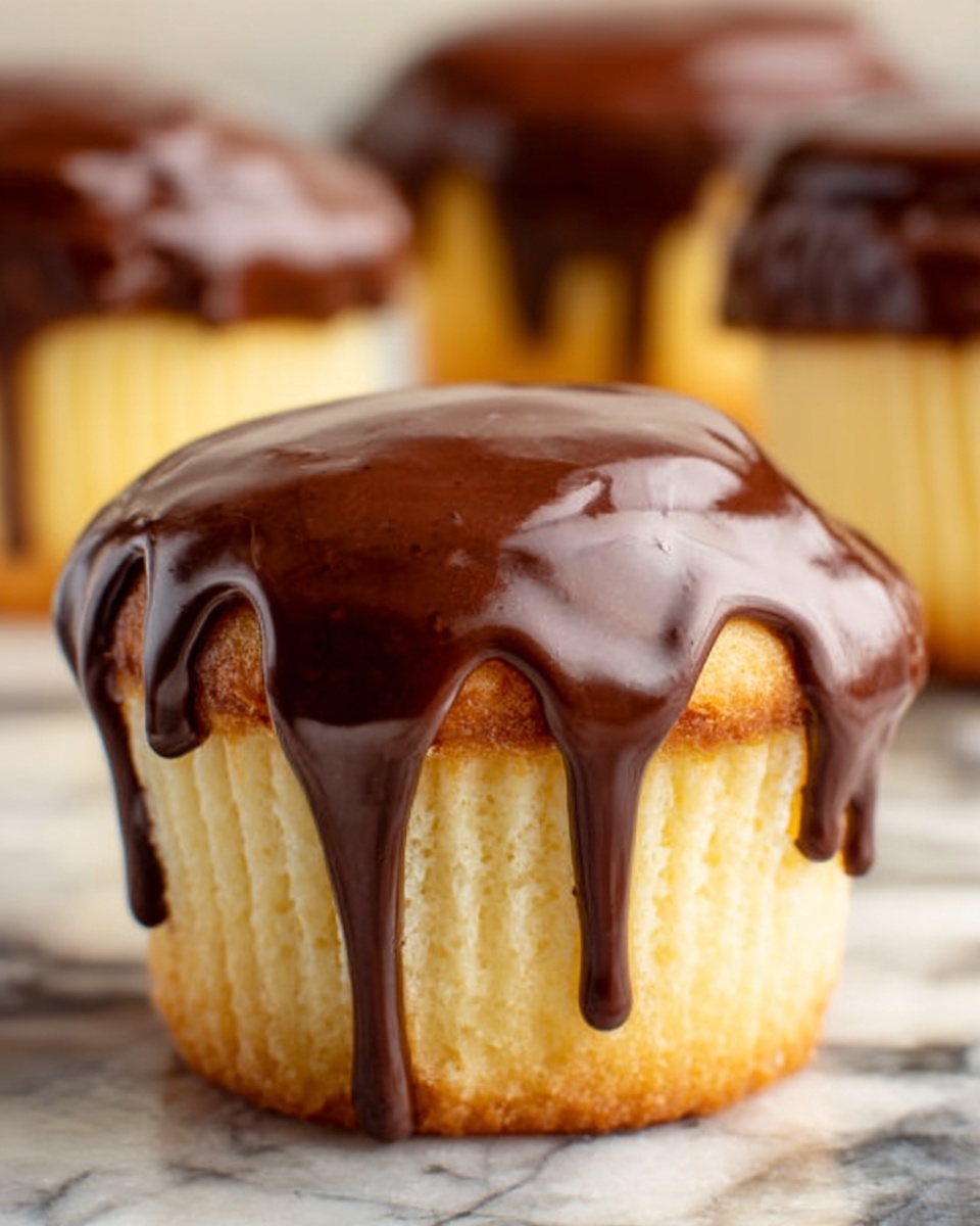 The image shows a close-up of a cupcake with three layers. The base is a light yellow cake with a smooth, soft texture. On top of the cake layer, there is a thick, shiny dark chocolate glaze that slowly drips down the sides. The glaze is glossy and rich, creating a contrast with the pale cake. In the background, there are blurred similar cupcakes atop a white marbled surface. The focus is mainly on the front cupcake, showing the detail of the chocolate layer dripping. photo taken with an iphone --ar 4:5 --v 7