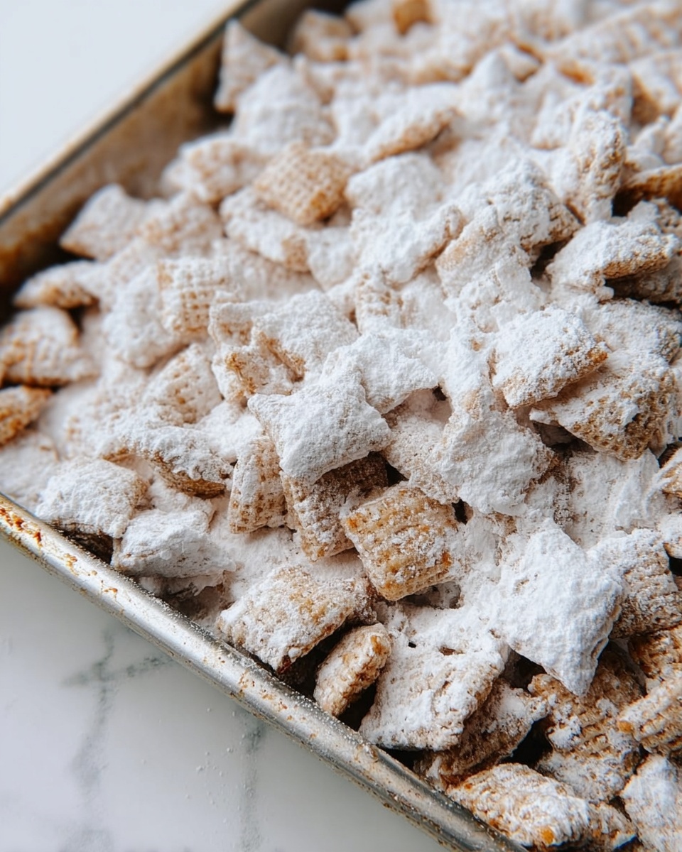 A close-up view of a metal baking pan filled with small square pieces of cereal coated heavily with a white powdered sugar layer. The cereal pieces are mostly light brown with a rough texture visible under the thick white powdered sugar, and the pan has worn edges adding a rustic look. The background is a white marbled texture. photo taken with an iphone --ar 4:5 --v 7