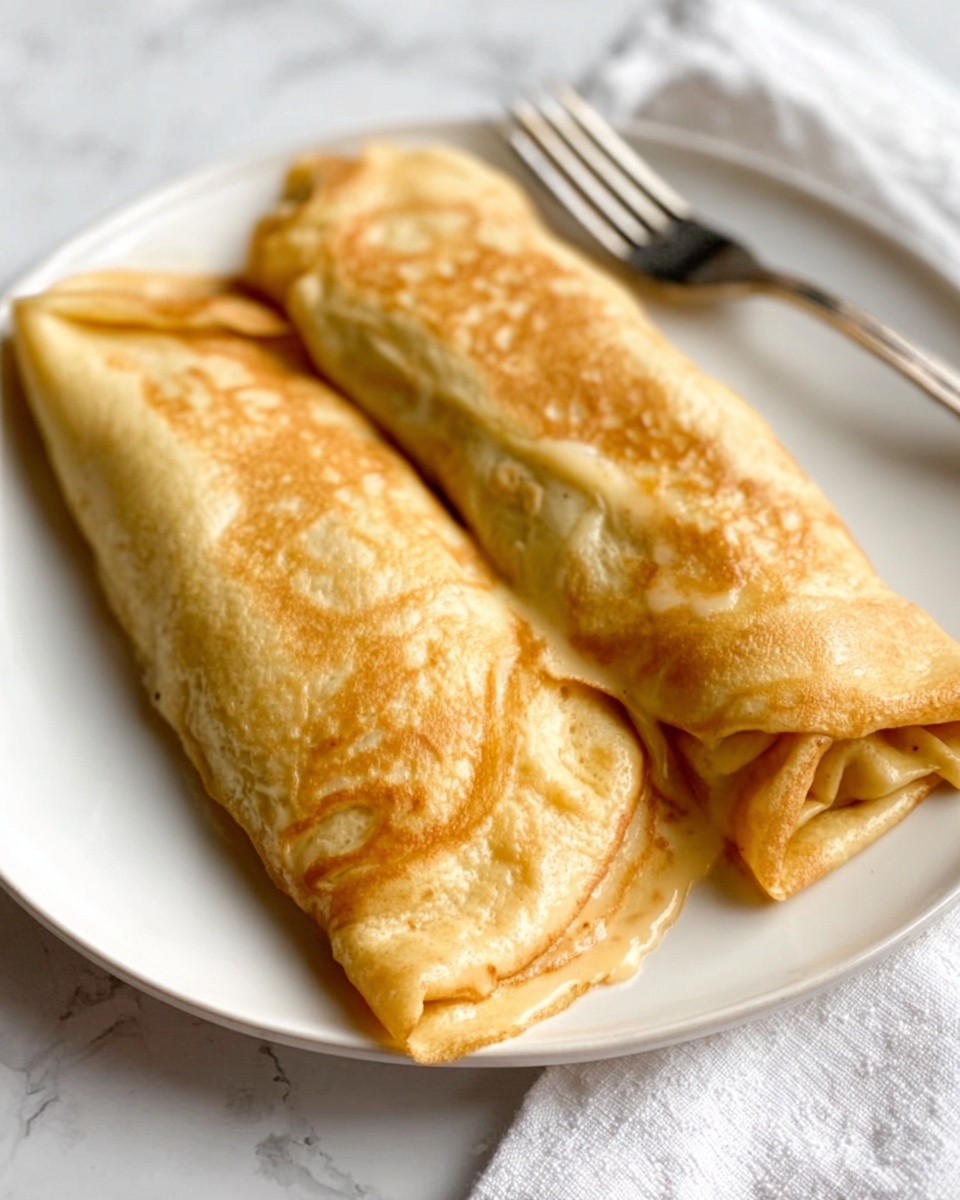 Two golden-brown rolled crepes are placed side by side on a white plate, each one showing a slightly shiny, smooth surface with a soft texture. The crepes have uneven, natural folds and are thick enough to reveal a gentle puffiness. The plate sits on a white marbled surface, with a silver fork to the right and a white cloth partially visible in the background. The lighting highlights the warm and inviting color of the crepes, giving a fresh, homemade feel to the dish. photo taken with an iphone --ar 4:5 --v 7