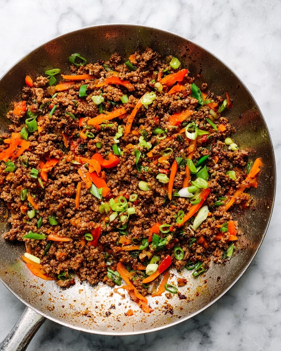 A close-up view of a metal pan filled with cooked ground meat mixed with small pieces of orange-red bell pepper, thin orange carrot strips, and green onion slices. The meat is brown and crumbly, and the vegetables add bright pops of color scattered evenly throughout the dish. The pan shows a shiny, slightly greasy texture with browned bits sticking to the sides. The whole scene is set on a white marbled surface. photo taken with an iphone --ar 4:5 --v 7