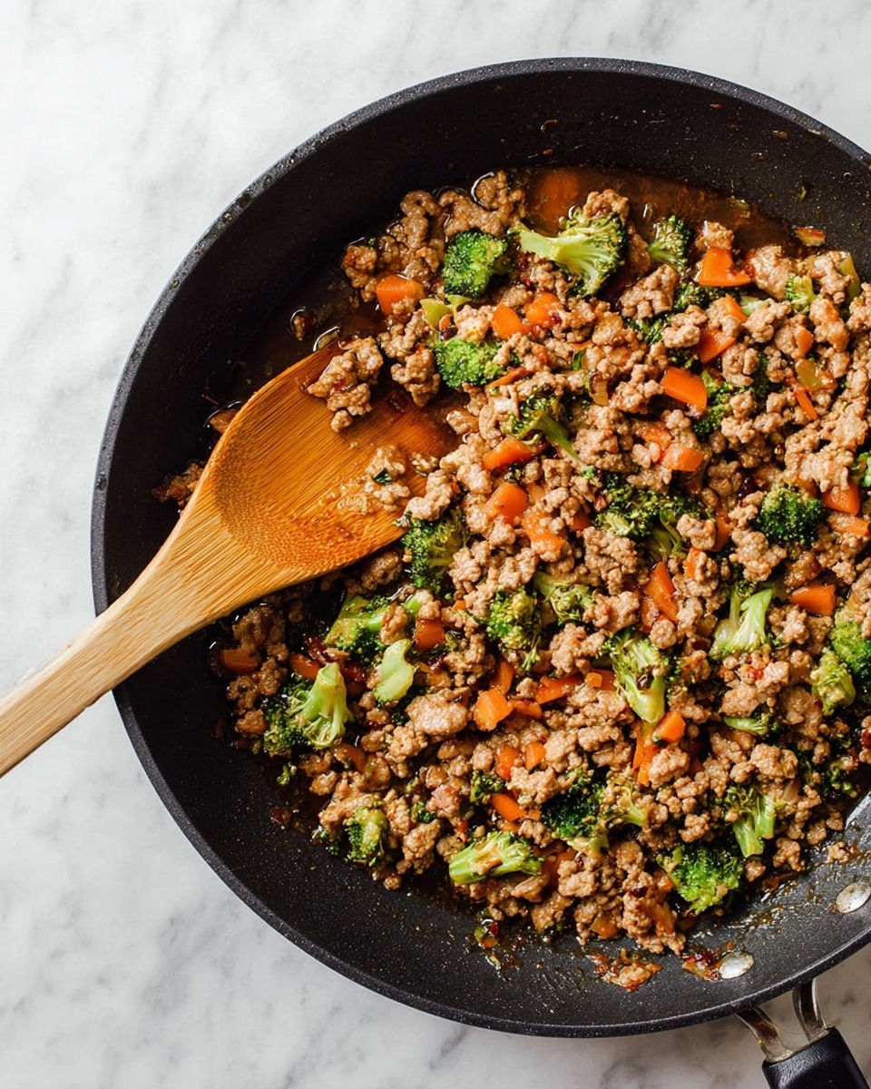 A black skillet filled with cooked ground meat mixed with small broccoli florets and thin orange carrot pieces, all coated in a glossy brown sauce. A wooden spoon is stirring the mixture from the left side of the skillet. The skillet is placed on a white marbled surface. photo taken with an iphone --ar 4:5 --v 7