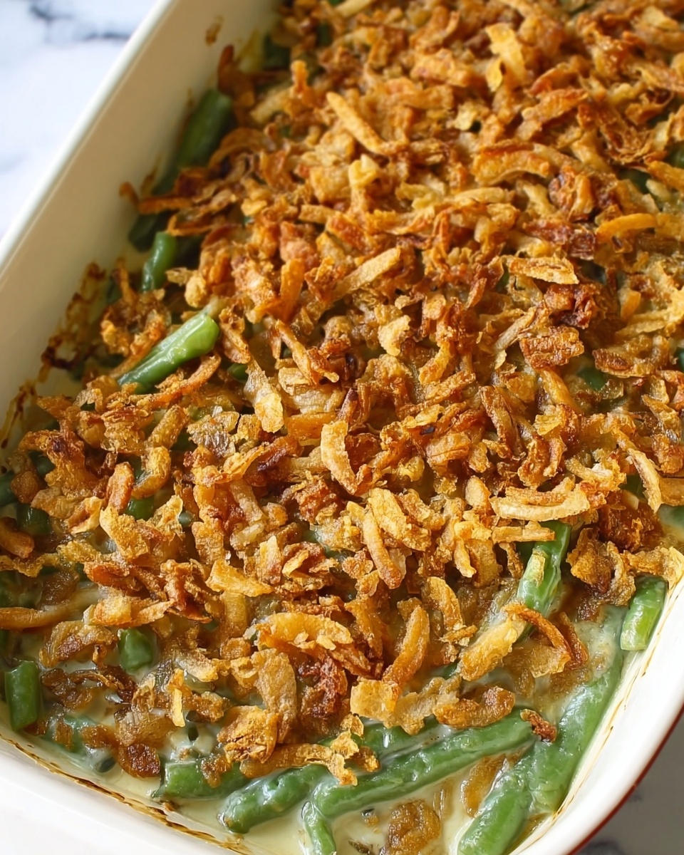The dish is a green bean casserole served in a white ceramic rectangular baking dish. The first layer at the bottom consists of green beans, visible through the edges, with a soft texture and green color. On top of the green beans, there is a creamy light beige sauce that slightly peeks through the crunchy topping layer. The top layer is a thick, golden-brown mix of crispy fried onions, scattered unevenly but completely covering the surface, providing a crunchy texture and a mix of light and dark brown hues. The dish is placed on a white marbled surface. photo taken with an iphone --ar 4:5 --v 7