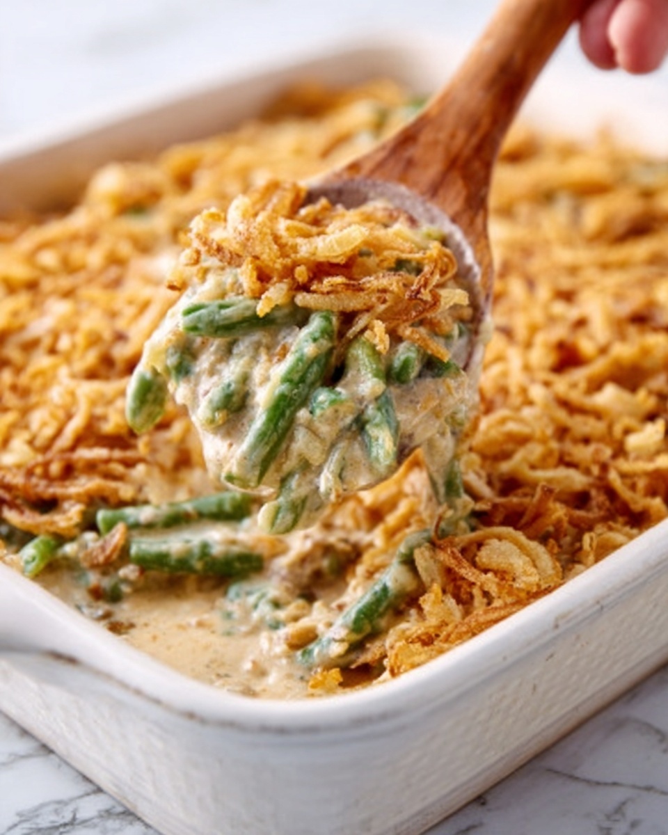 The image shows a white rectangular dish filled with a creamy green bean casserole. The casserole has one visible layer of green beans mixed with a thick creamy white sauce, topped with a golden brown crispy fried onion layer. A wooden spoon held by a woman's hand is scooping a portion, showing the creamy and slightly textured mix of green beans and sauce underneath the crispy topping. The dish is set on a white marbled surface. photo taken with an iphone --ar 4:5 --v 7