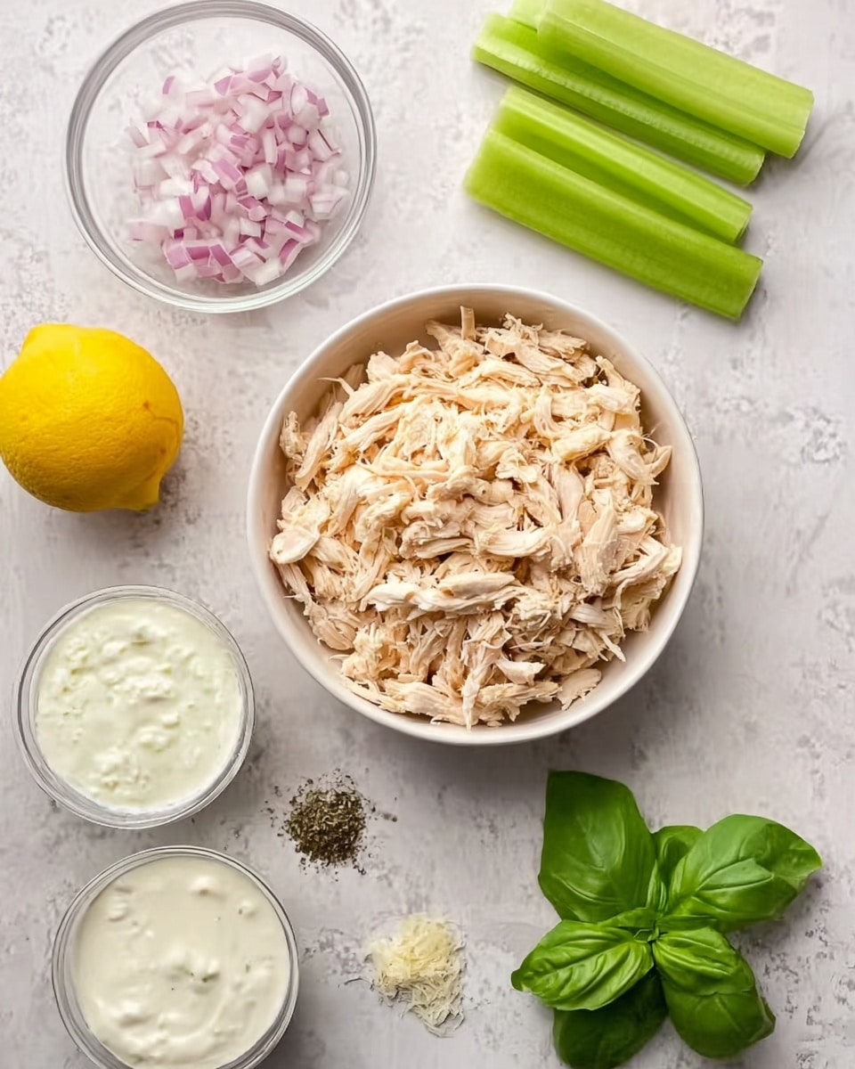 A white bowl filled with shredded cooked chicken, placed on a white marbled surface. Nearby, there is a whole yellow lemon on the right, a small glass bowl of chopped red onion above two celery sticks lying side by side, and a small clove of garlic below them. Two small glass bowls contain white creamy sauces, and fresh green basil leaves are placed at the bottom right. Black pepper is sprinkled on the surface near the garlic. Photo taken with an iphone --ar 4:5 --v 7