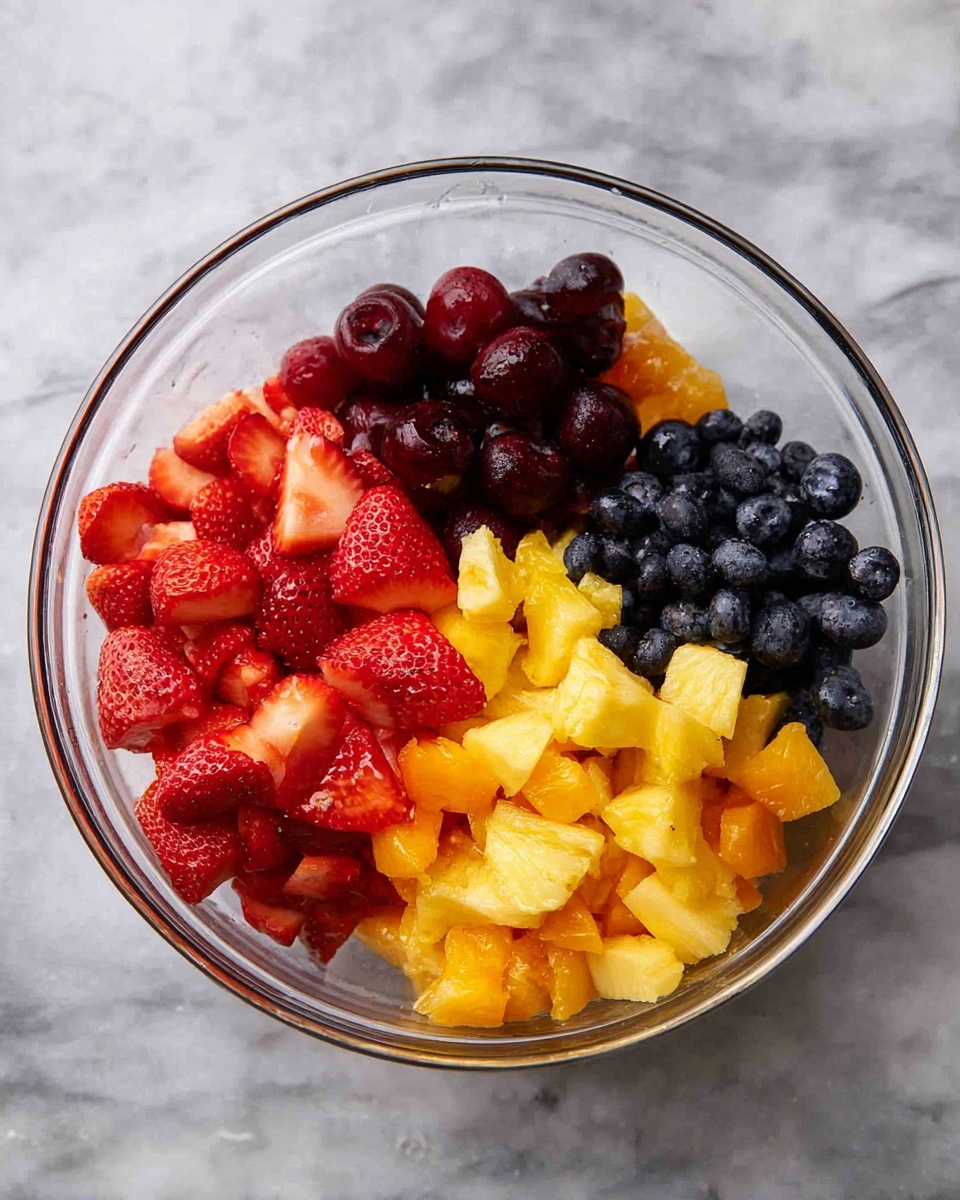 A clear glass bowl on a white marbled surface holds a colorful fruit mix divided into four main sections: the bottom left has bright red, halved strawberries with visible seeds and juicy texture; the bottom center-right contains dark red cherries mixed with yellow chunks that look like pineapple; the top right features yellow and orange peach or nectarine pieces with soft, slightly shiny flesh; the top left has small round, deep blue blueberries with a smooth texture. The fruits are fresh and arranged neatly, showing a variety of shapes and colors, with no mixing between the sections photo taken with an iphone --ar 4:5 --v 7