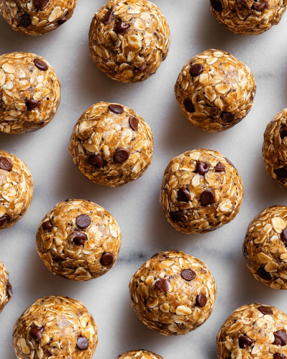 The image shows many round energy bites placed close together on a white marbled surface. Each bite is made from layers of light brown oats mixed with small, darker brown chocolate chips spread unevenly throughout. The oats have a rough texture, and the chocolate chips add small smooth patches on the surface of each round bite. The bites have a uniform size and shape, arranged in a loose grid pattern across the frame. photo taken with an iphone --ar 4:5 --v 7