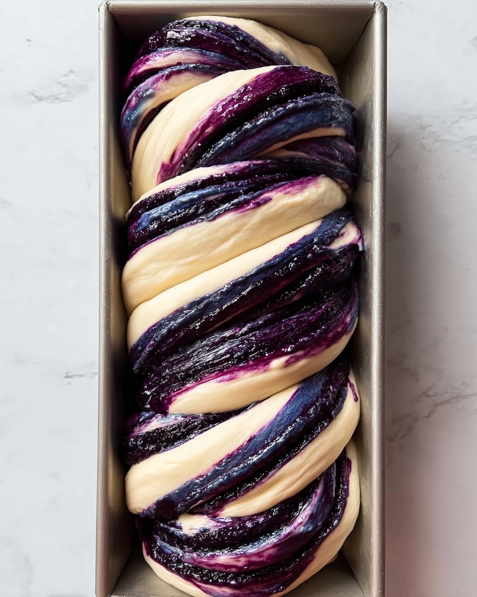 A loaf of twisted bread dough is shown from above in a rectangular baking pan filled with thick swirls of dark purple and deep blue filling. The dough is pale cream colored, smooth, and soft, wrapping around the filling in alternating thick layers that reveal a braided pattern. The filling has a shiny, slightly textured surface, contrasting with the smooth dough, and spreads evenly in wide bands that twist throughout the loaf. The baking pan is placed on a surface with a white marbled texture. photo taken with an iphone --ar 4:5 --v 7