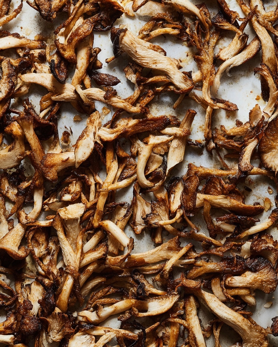 A close-up image of many thin, uneven strips of cooked mushrooms spread out flat on a metal pan. The strips vary in color from light brown to dark brown with some crispy, almost blackened edges. The texture looks rough and slightly shiny, showing a mix of tender and crispy parts. The mushrooms are layered randomly, overlapping each other across the entire pan surface, with bits of small browned garlic or seasoning scattered throughout. The background is a white marbled texture. photo taken with an iphone --ar 4:5 --v 7