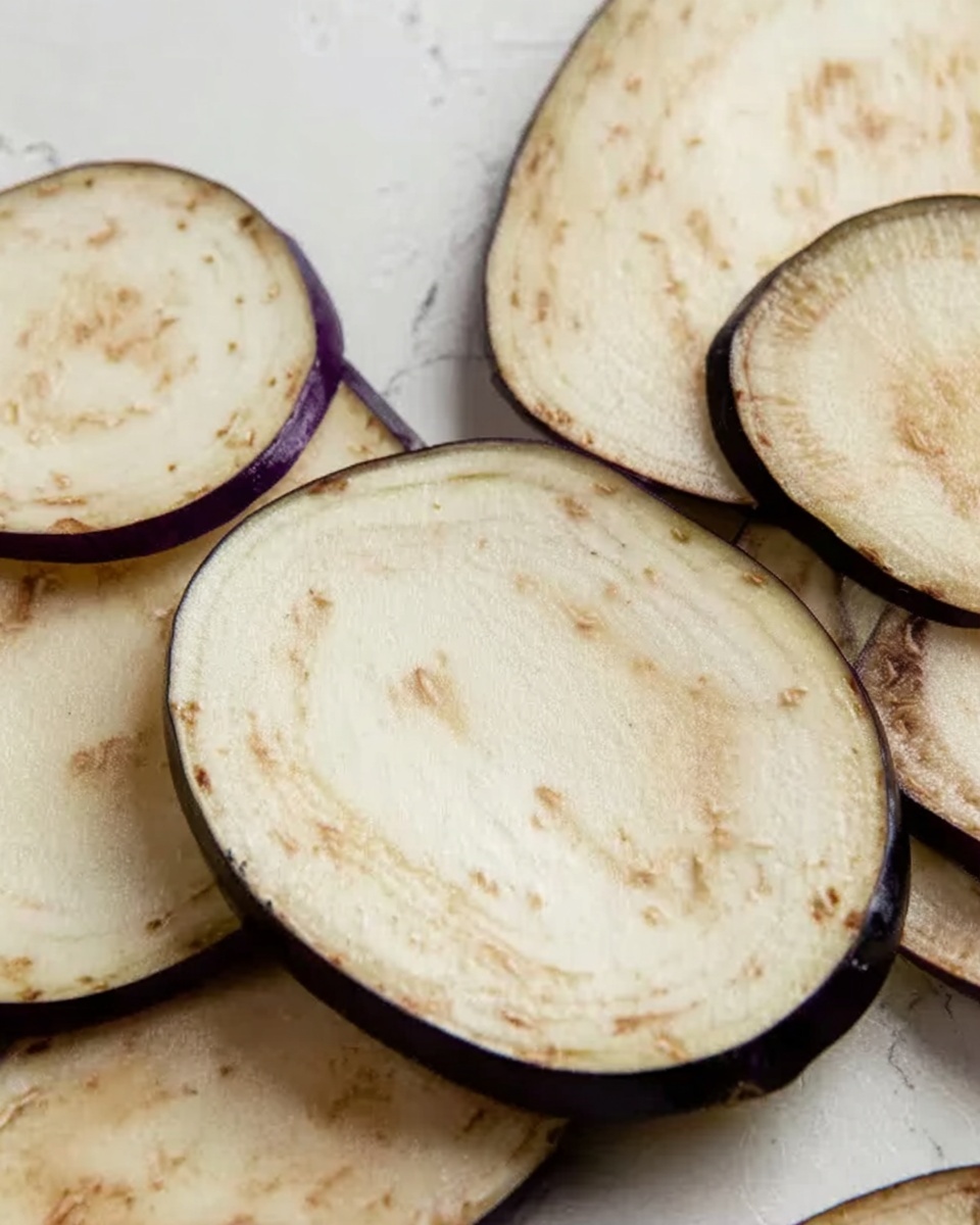 The image shows several thin slices of eggplant arranged unevenly on a clean white marbled surface. The eggplant slices have a light beige color on the inside with small light brown seeds visible, and their edges are dark purple with a smooth texture. The slices overlap slightly in some areas, showing their soft, moist texture. The overall light and natural tones of the eggplants contrast softly with the clean white marbled background. photo taken with an iphone --ar 4:5 --v 7