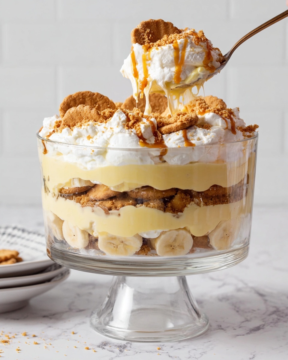 The image shows a tall glass trifle dish on a clear pedestal filled with multiple layers of dessert. From the bottom up, the first layer is light yellow pudding, smooth and creamy in texture. Above that is a layer of round beige cookies or crackers, partially soaked. A second, thicker layer of the same light yellow pudding follows, topped with a layer of round banana slices. Above the bananas, there is a thin layer of cookies or crackers again, partly covered by a thick fluffy white topping, likely whipped cream. The top is finished with a sprinkle of crumbled cookies and drizzled caramel sauce. A spoon lifting a scoop of the dessert reveals the same layers, showcasing the creamy, crumbly, and smooth textures in a light and warm color palette against a white marbled surface. Photo taken with an iphone --ar 4:5 --v 7