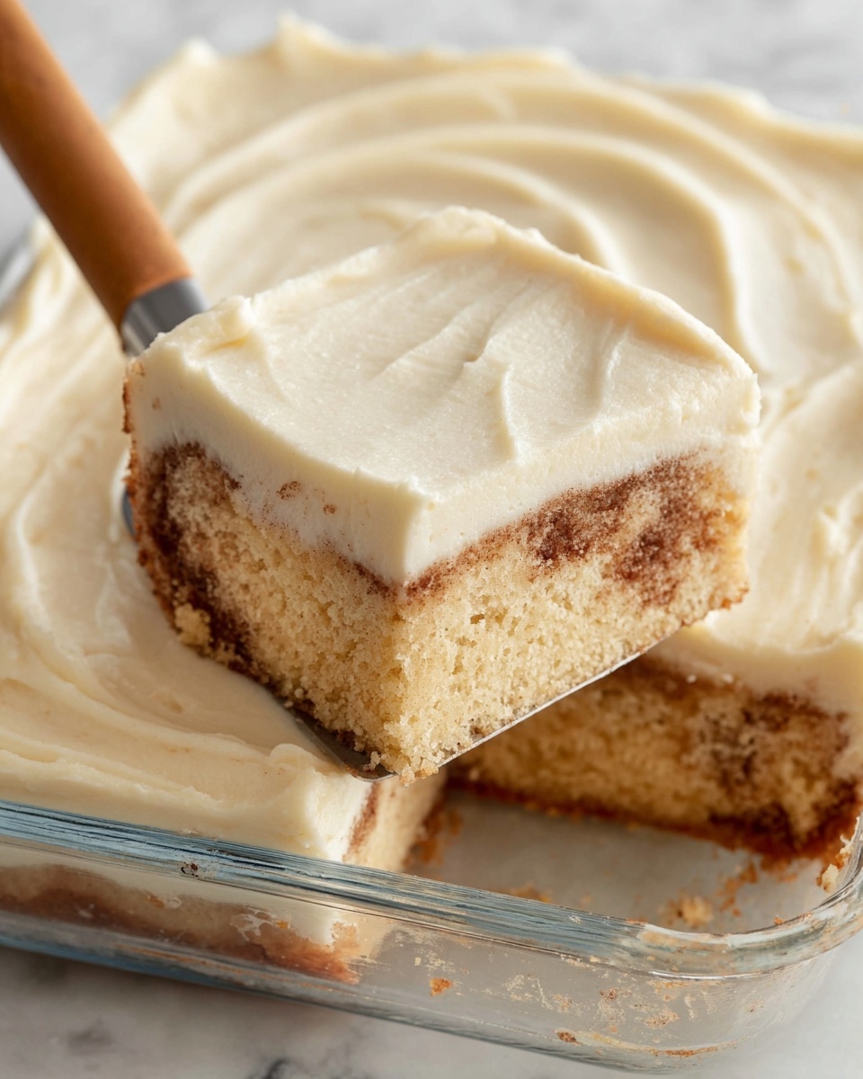 The image shows a close-up of a square piece of cinnamon swirl cake with two visible layers. The bottom layer is light beige with swirled brown cinnamon spots, giving a soft, fluffy texture. The top layer is a thick, smooth, creamy white frosting that evenly covers the cake with gentle, curved spatula marks. The cake piece is slightly lifted by a spatula with a wooden handle from a clear glass baking dish. The background is a white marbled surface. photo taken with an iphone --ar 4:5 --v 7