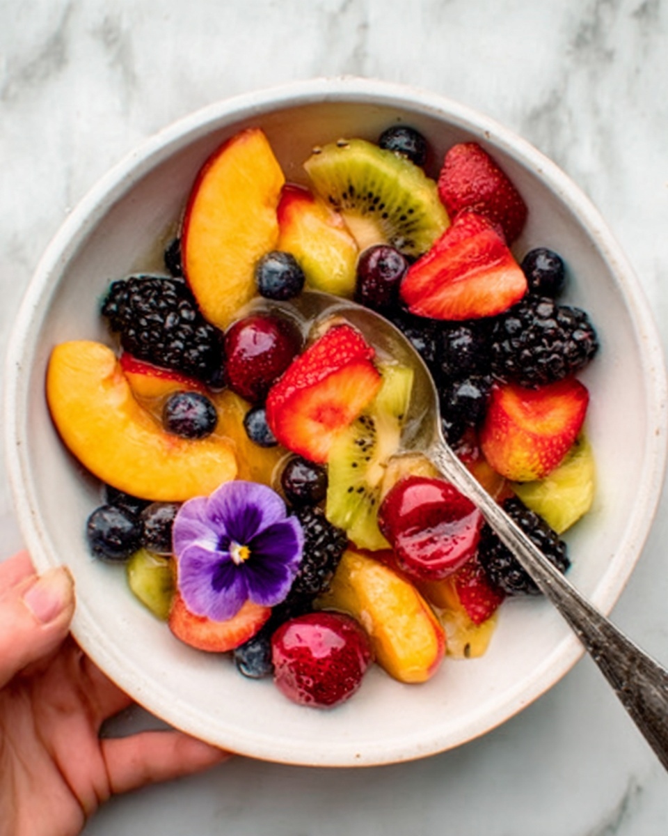 The image shows a white bowl filled with a colorful fruit salad on a white marbled surface. The fruit pieces include bright orange peach slices, red strawberries, dark purple grapes, rich blackberries, and yellow kiwi with small black seeds scattered on top. A silver spoon rests inside the bowl, holding some of the fruit mixed together, while a small purple edible flower decorates the side. A woman's hand is gently holding the bowl, showing part of the thumb and fingers. photo taken with an iphone --ar 4:5 --v 7