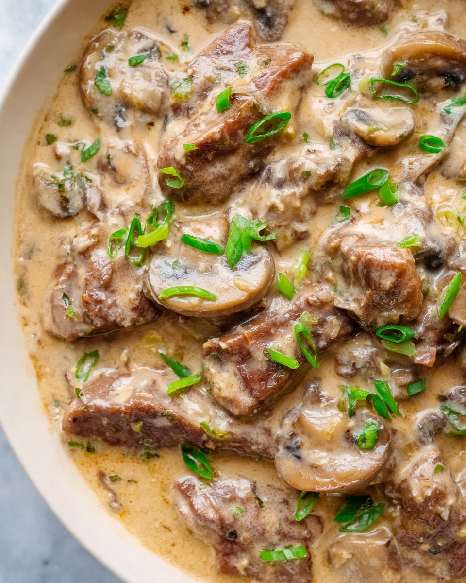 The image shows a close-up view of a creamy dish with several thick slices of cooked meat and mushrooms evenly mixed in a rich, light beige sauce. The sauce looks smooth with a slightly glossy texture and is dotted with small green onion pieces scattered on top, adding a fresh color contrast. The meat slices have a browned, tender look, and the mushrooms are soft, blending well into the creamy sauce. The whole dish is set against a white marbled surface, giving a clean and bright background. photo taken with an iphone --ar 4:5 --v 7