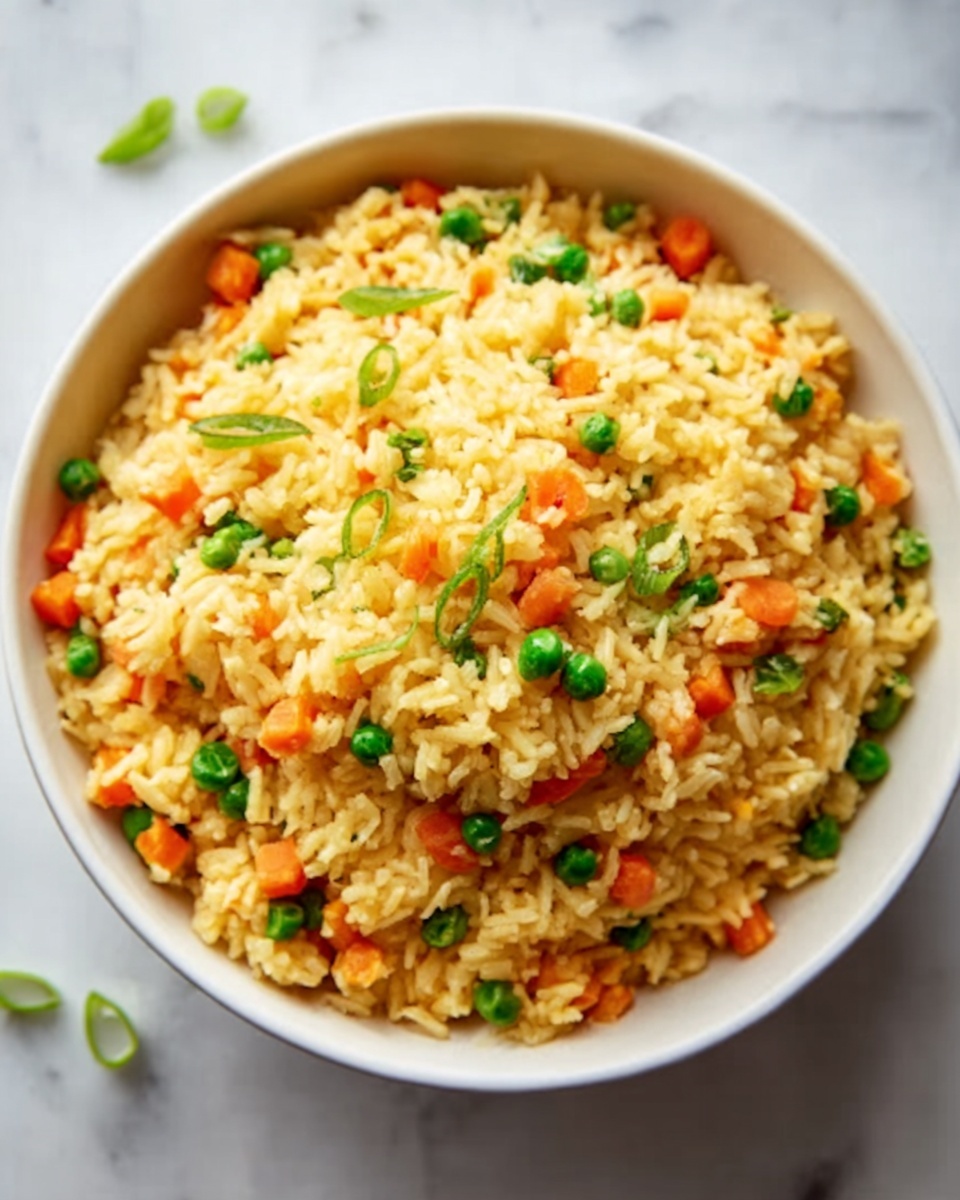 The image shows a close-up of fried rice in a dark speckled pan, with visible pieces of cooked chicken scattered throughout. The rice is golden-brown, mixed evenly with small chunks of bright orange carrots and green peas. There are bits of scrambled egg mixed in, adding a soft yellow layer among the grains. Fresh green chopped onions are sprinkled on top, adding a pop of color and freshness to the texture. The handle of a wooden spoon is partially visible, stirring the mixture against a white marbled surface. The scene has a warm, home-cooked feel. photo taken with an iphone --ar 4:5 --v 7