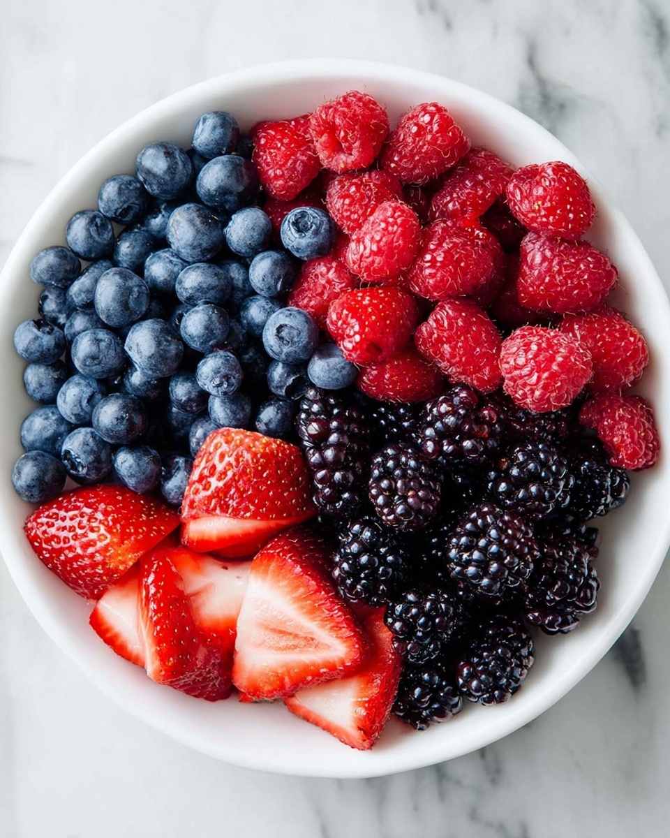 A white bowl filled with four sections of fresh berries arranged neatly in layers: the top left layer has dark blue, round blueberries with a smooth texture; the top right layer is red raspberries with a bumpy surface; the bottom right layer is deep blackish-purple blackberries, glossy and textured; the bottom left layer has red strawberries, sliced to show their pale inner flesh and seeds on the surface. The bowl is placed on a white marbled surface. photo taken with an iphone --ar 4:5 --v 7