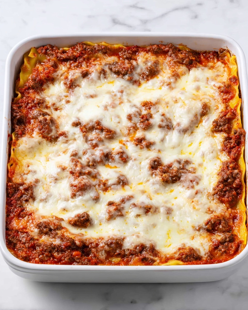 The image shows a square white baking dish filled with a lasagna. The bottom layer is a rich red tomato sauce mixed with bits of cooked ground meat, visible through small gaps. Above this, there is a layer of yellow pasta sheets, partly covered by the sauce and meat mixture. The top layer is thick melted cheese that is creamy white with golden brown spots, spread evenly across the whole surface with some areas showing the sauce underneath. The dish sits on a white marbled surface. photo taken with an iphone --ar 4:5 --v 7