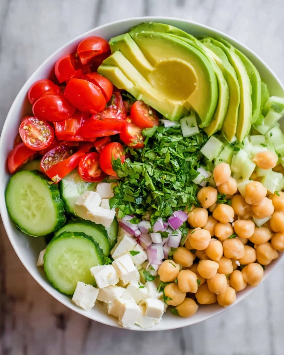 A white bowl filled with six neat sections of fresh ingredients arranged in a circle. One section has light green slices of avocado with a smooth texture, next to bright red cherry tomato halves with shiny skin. Another section shows small red tomato pieces, while beside them are small white cubes of cheese with a crumbly texture. There is a bunch of fresh, finely chopped green herbs in the center, surrounded by slices of cucumber with a pale green peel and light flesh. The last section contains round, beige chickpeas with a smooth surface. The bowl is placed on a white marbled surface. photo taken with an iphone --ar 4:5 --v 7