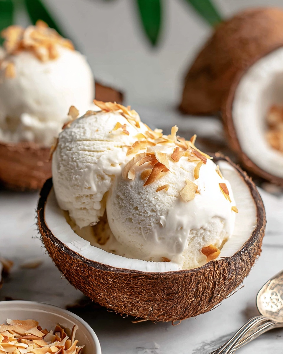 Two scoops of white creamy coconut ice cream with a smooth texture are placed inside a brown textured coconut shell half. The ice cream is topped with small pieces of toasted coconut flakes, adding a bit of light brown color and crunch on top. The white coconut shell lining is visible around the ice cream. In the background, there are more brown coconut halves and a small bowl filled with toasted coconut flakes. Everything is set on a white marbled surface, and a silver spoon with a detailed handle rests nearby. photo taken with an iphone --ar 4:5 --v 7