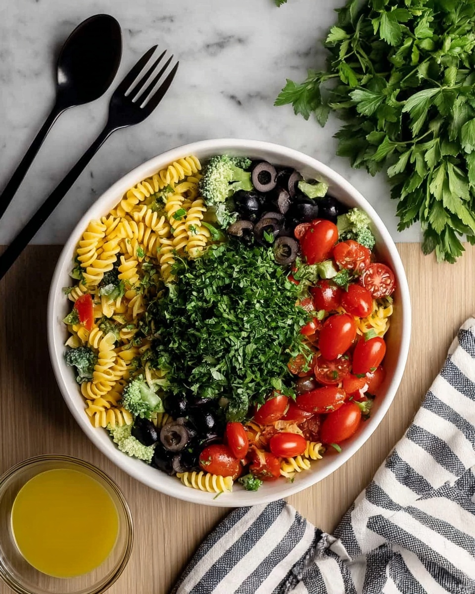 A white bowl filled with a pasta salad showing four main layers: the bottom layer is yellow spiral pasta, above it is a mix of small green broccoli pieces, followed by scattered black olive slices and whole red cherry tomatoes, and the top layer is a large pile of finely chopped dark green parsley in the center. The bowl is set on a white marbled surface, with a black fork and spoon placed above it on the left, some fresh green parsley sprigs on the upper right, a striped white and black cloth to the right, and a glass bowl of yellow dressing below on the left. photo taken with an iphone --ar 4:5 --v 7
