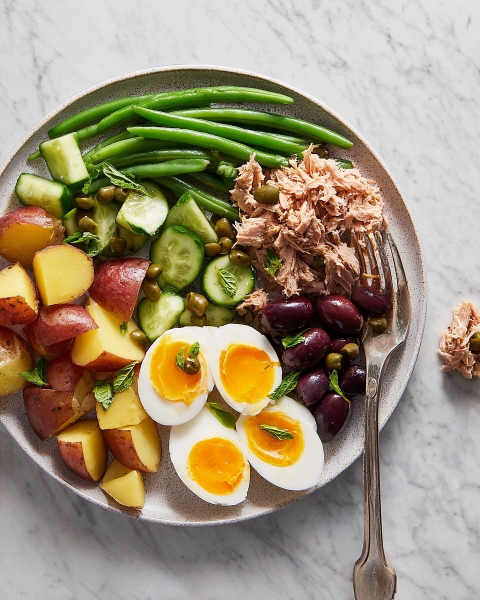 A white plate sits on a white marbled surface, filled with a colorful salad arranged in sections. Starting from the top left and moving clockwise, there are pale yellow artichoke hearts, bright red cherry tomatoes and kalamata olives in dark purple, shredded light pink tuna in the center, more cherry tomatoes on green lettuce, six slices of boiled eggs showing bright yellow yolks and white edges, a small pile of white mozzarella balls with green herbs, lemon wedge slices, light yellow boiled potatoes, a bunch of green beans pointing upward from the bottom center, red rings of roasted bell peppers, and more dark purple kalamata olives scattered near the boiled eggs and red pepper. The whole salad is sprinkled lightly with dried herbs. photo taken with an iphone --ar 4:5 --v 7