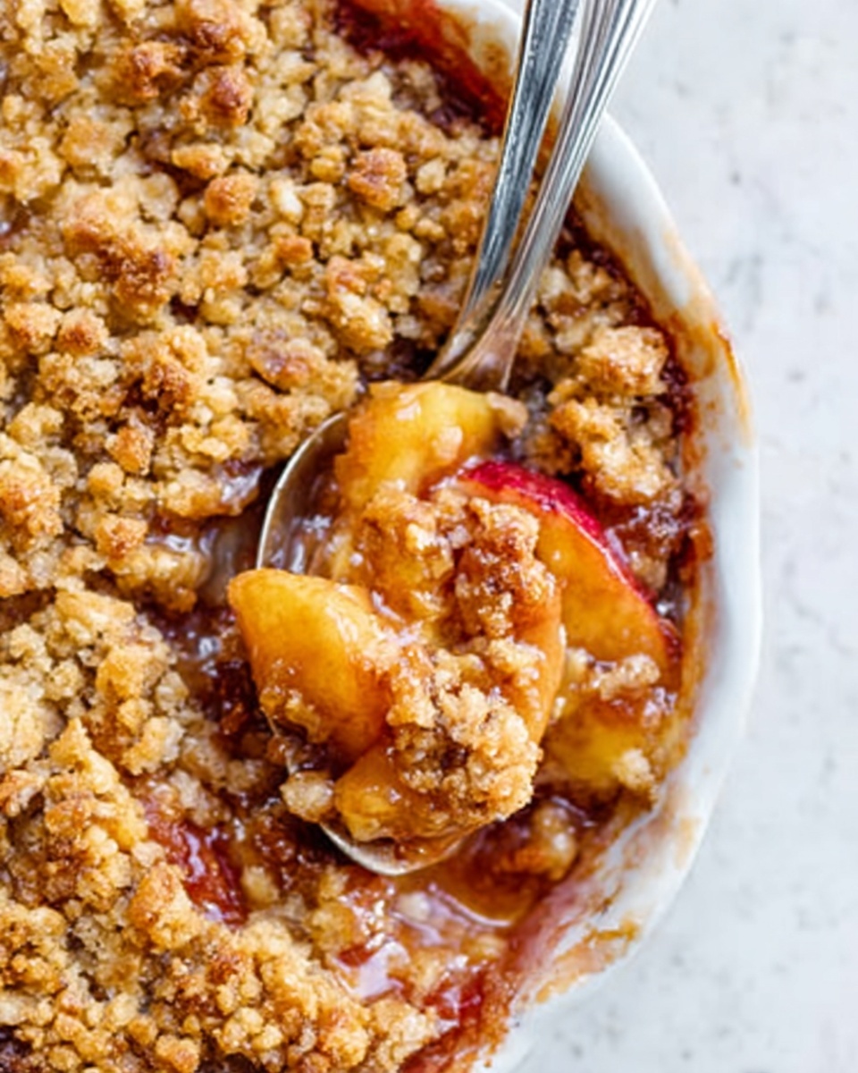 The image shows a close-up of a dessert with a crumbly, golden brown topping that has a rough, crunchy texture covering soft, warm fruit pieces underneath. There are two silver spoons partially buried in the dessert, each holding some of the fruit and crumb mixture, with a shiny, caramelized glaze on the fruit giving it a glossy look. The dessert is in a white dish, and it sits on a white marbled textured surface. The photo is bright and sharp, highlighting the rich textures and warm colors of the dish. photo taken with an iphone --ar 4:5 --v 7
