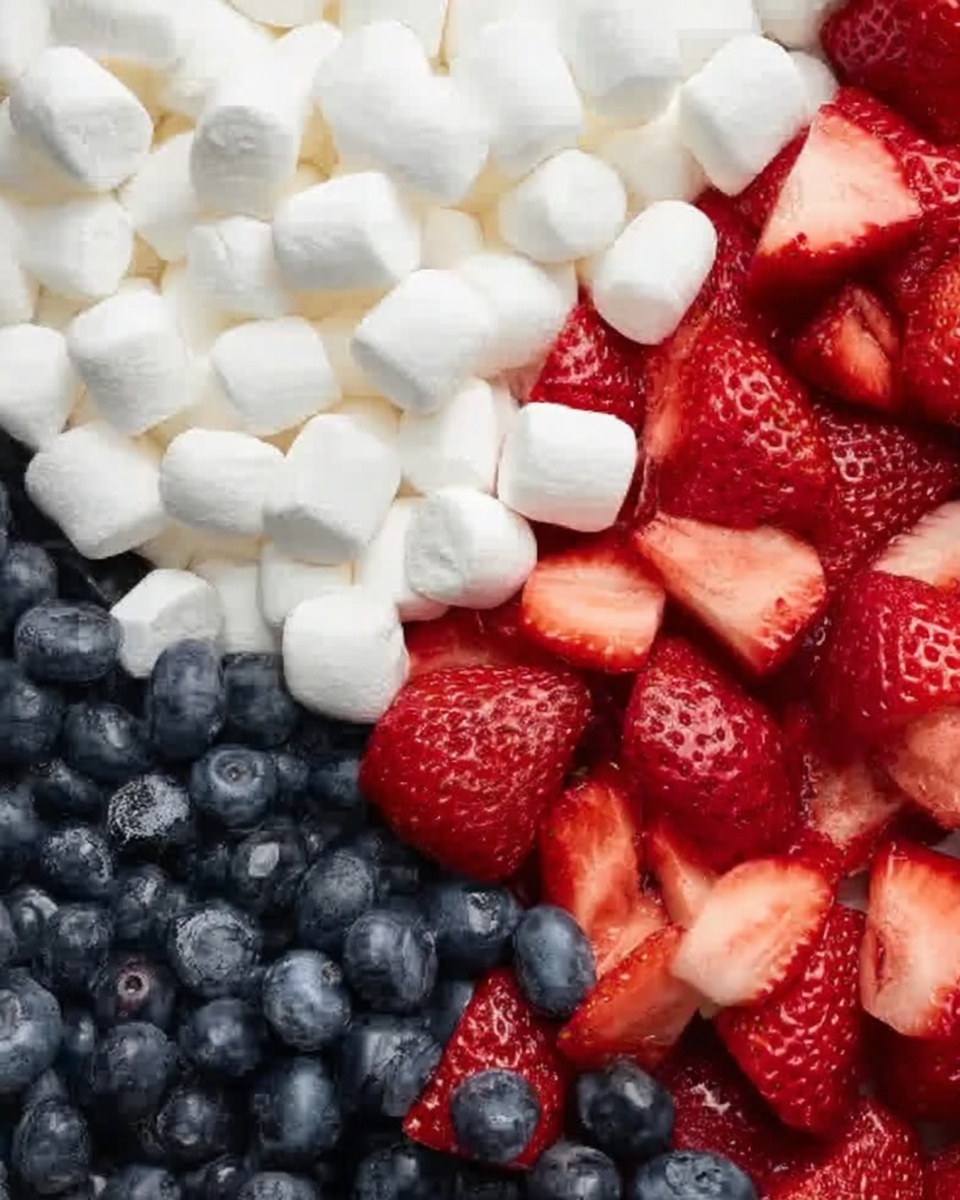 The image shows a close-up of three clear sections on a white marbled surface, each filled with different fruits and marshmallows. At the top is a thick layer of small white marshmallows, soft and smooth. Below them, on the right, are fresh, bright red strawberries, sliced into uneven pieces with a slightly glossy texture. On the left side are round, dark blue blueberries, tightly packed and shiny. The colors contrast well, with the white marshmallows, red strawberries, and blue blueberries creating a fresh and colorful look. Photo taken with an iphone --ar 4:5 --v 7