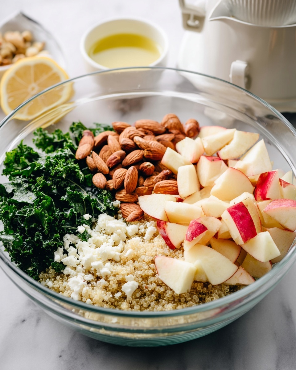A clear glass bowl on a white marbled surface holds a layered salad: the bottom layer is light beige cooked quinoa, topped on one side with dark green chopped kale leaves. Next to the kale, there is a cluster of whole and chopped brown almonds. On the other side is a pile of small white crumbled cheese, and on top of everything, there are diced red and white apples. In the background, out of focus, there is a white citrus juicer with a lemon half and a small white bowl with light yellow liquid. Photo taken with an iphone --ar 4:5 --v 7