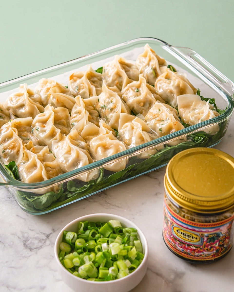 A clear glass rectangular dish holds three neat rows of dumplings, each with a light golden to pale color and a slightly crispy texture on top. Underneath the dumplings, fresh green spinach leaves add a layer of bright green. In the foreground, a small white bowl is filled with chopped green onions, showing vibrant green rings. Next to the bowl, a jar with a gold lid and colorful label is placed on a smooth white marbled surface. The whole scene is lit softly and has a clean and fresh look. photo taken with an iphone --ar 4:5 --v 7