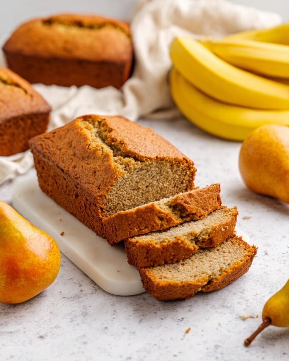 A loaf of banana bread sits on a small white cutting board placed on a white marbled surface. The loaf is golden brown with a cracked top crust and is sliced into five pieces, showing a moist, dense inside with a slightly coarse texture. Two whole loaves of banana bread are placed on a white cloth behind the cutting board. To the right of the cutting board is a yellow bunch of bananas, and a ripe orange pear with a brown stem is near the bottom right. Another similar pear is partly visible to the left. The scene has soft natural lighting. photo taken with an iphone --ar 4:5 --v 7