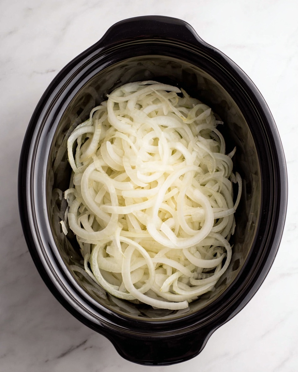 Slow Cooker French Onion Soup Recipe 4 A black slow cooker filled with one thick layer of thinly sliced white onions spread evenly inside. The onions have a soft, pale yellow-white color and a smooth, slightly translucent texture. The slow cooker is placed on a white marbled surface. photo taken with an iphone --ar 4:5 --v 7