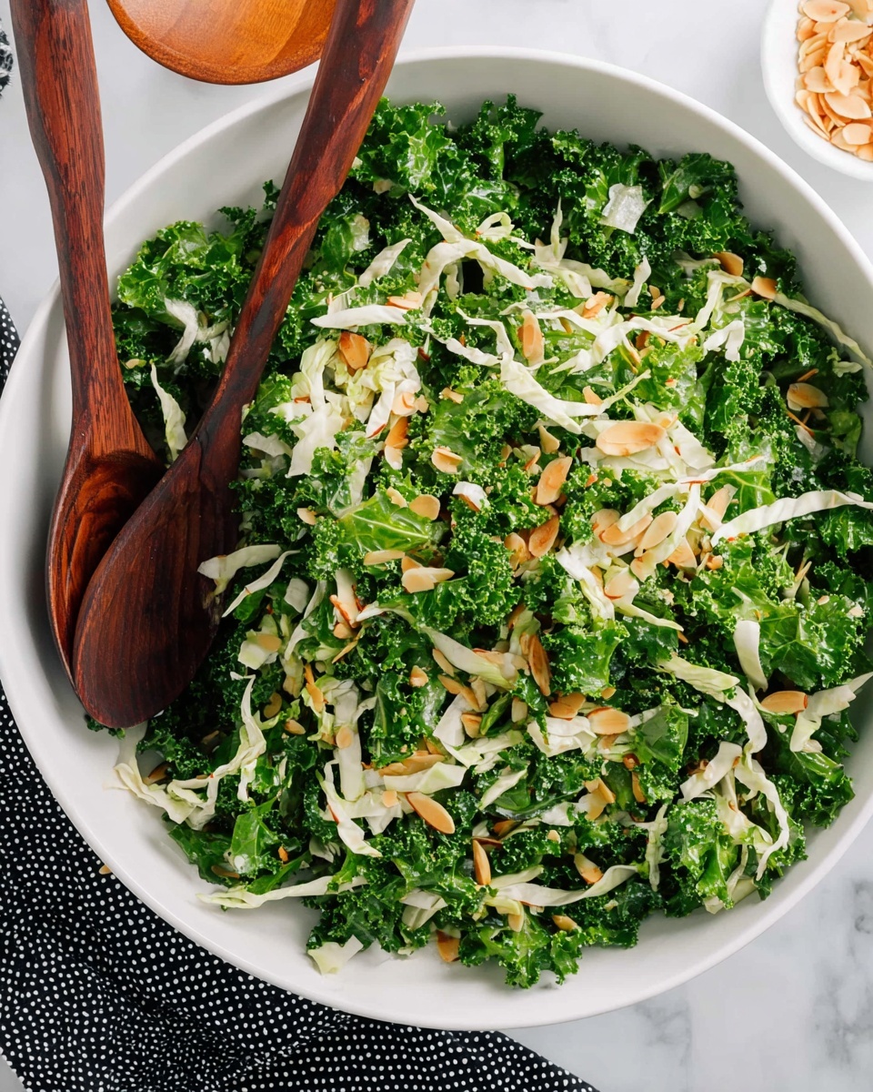 The image shows a large white bowl filled with fresh kale salad. The salad has a base layer of dark and light green curly kale leaves, mixed with thin, pale strips of cabbage evenly spread on top. Scattered on the salad are small golden brown almond slivers adding a crunchy texture. Two dark wooden salad spoons rest inside the bowl on the left side. The bowl is placed on a white marbled surface with a black and white dotted cloth partially visible. Photo taken with an iphone --ar 4:5 --v 7