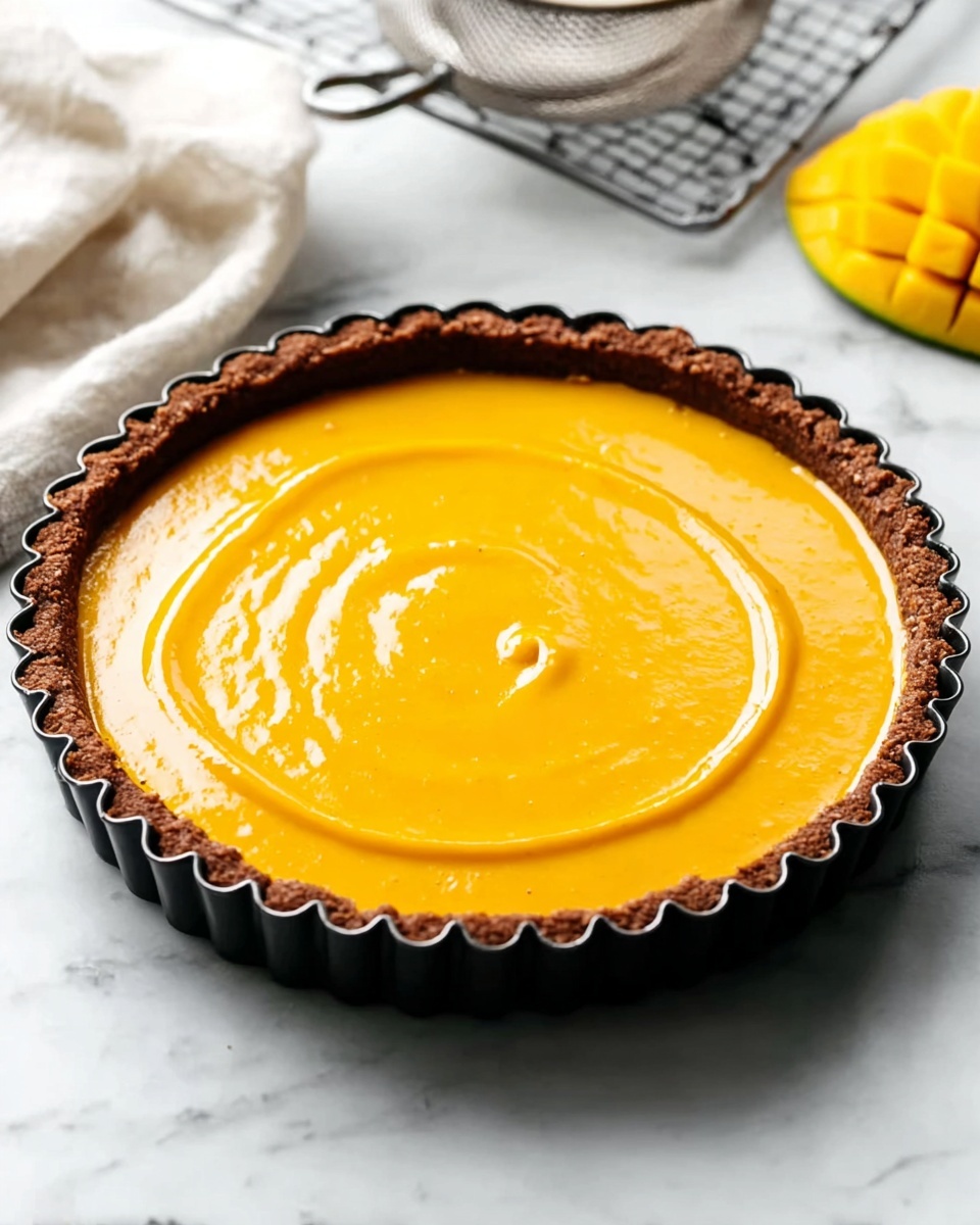 Asian Cucumber Salad TikTok Recipe 5 A round tart with a golden brown crumbly crust as the bottom and sides, filled with a smooth, bright orange filling that has a glossy surface with soft spiral swirls from the center outwards. The tart is in a fluted white pie dish placed on a white marbled surface, with a metal sieve and a yellow sliced mango blurred in the background. Photo taken with an iphone --ar 4:5 --v 7