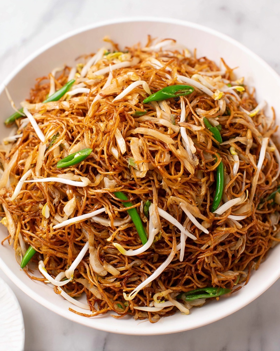 A large white bowl filled with thin golden-brown noodles, mixed with white bean sprouts and scattered green chili peppers on top. The noodles are slightly shiny, showing a light sauce coating, and have a textured, tangled look. A white marbled surface is under the bowl with some blurred white containers in the background. photo taken with an iphone --ar 4:5 --v 7
