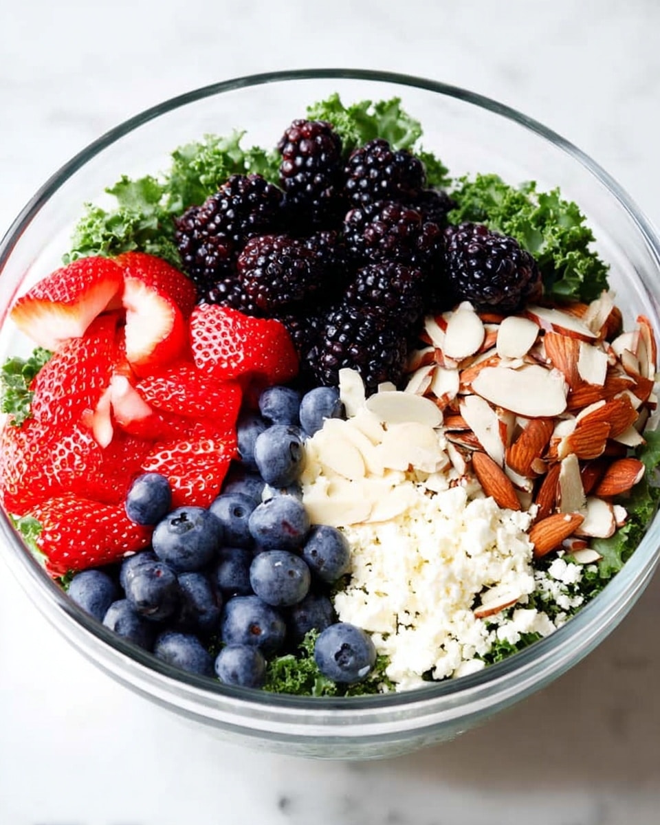 A clear glass bowl shows a fresh salad made in layers: a green leafy kale base at the bottom, topped with four sections of colorful ingredients. One section has black blackberries with a shiny texture, next to them bright red sliced strawberries, then blue round blueberries, and finally pale sliced almonds mixed with white crumbled cheese. The bowl sits on a white marbled surface photo taken with an iphone --ar 4:5 --v 7