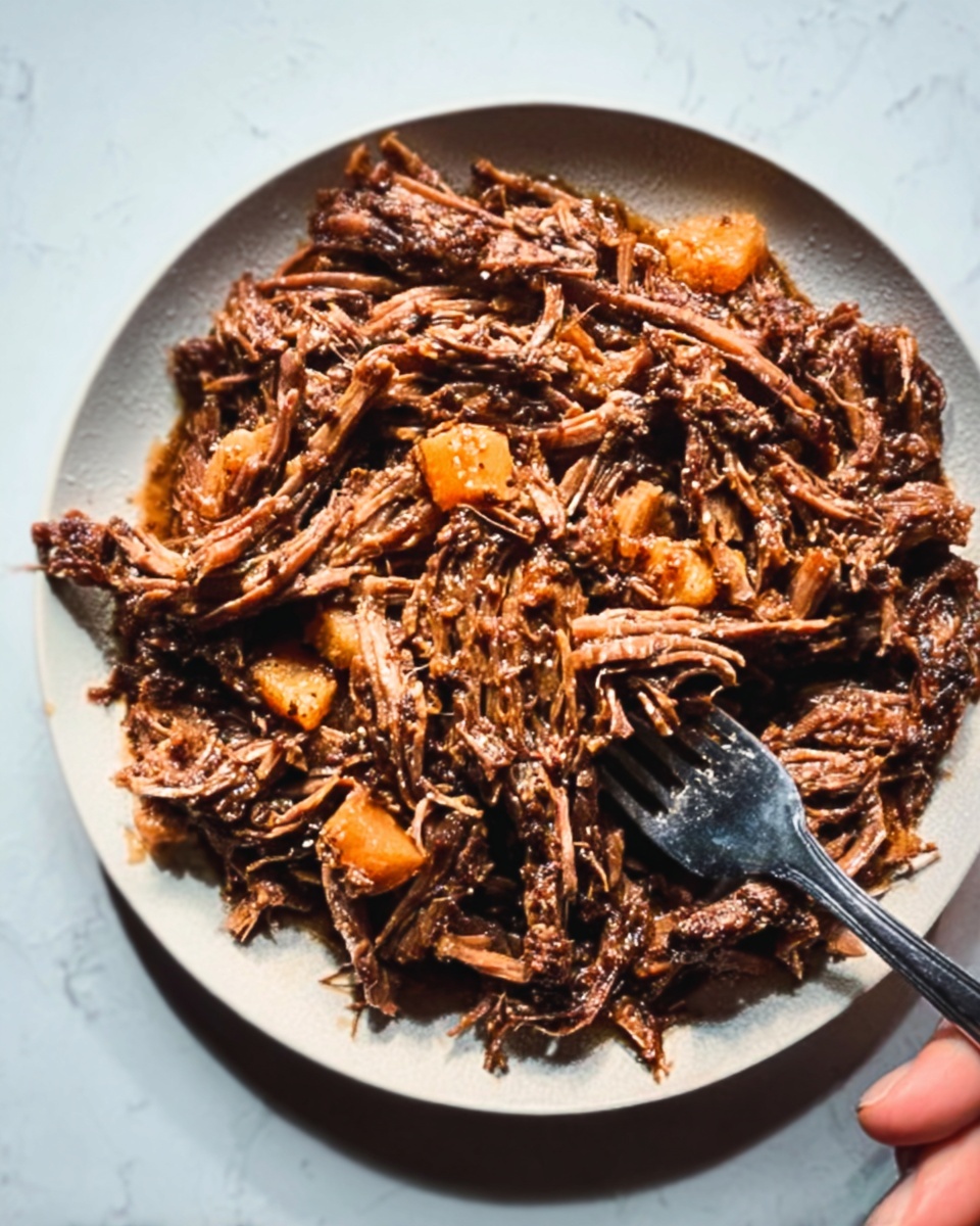 A white plate filled with shredded cooked meat mixed with small orange chunks that look soft, all covered in a rich brown sauce with a slightly glossy texture. A silver fork is placed on the right side into the food, and a woman's hand is gently holding the edge of the plate. The plate sits on a white marbled surface. photo taken with an iphone --ar 4:5 --v 7